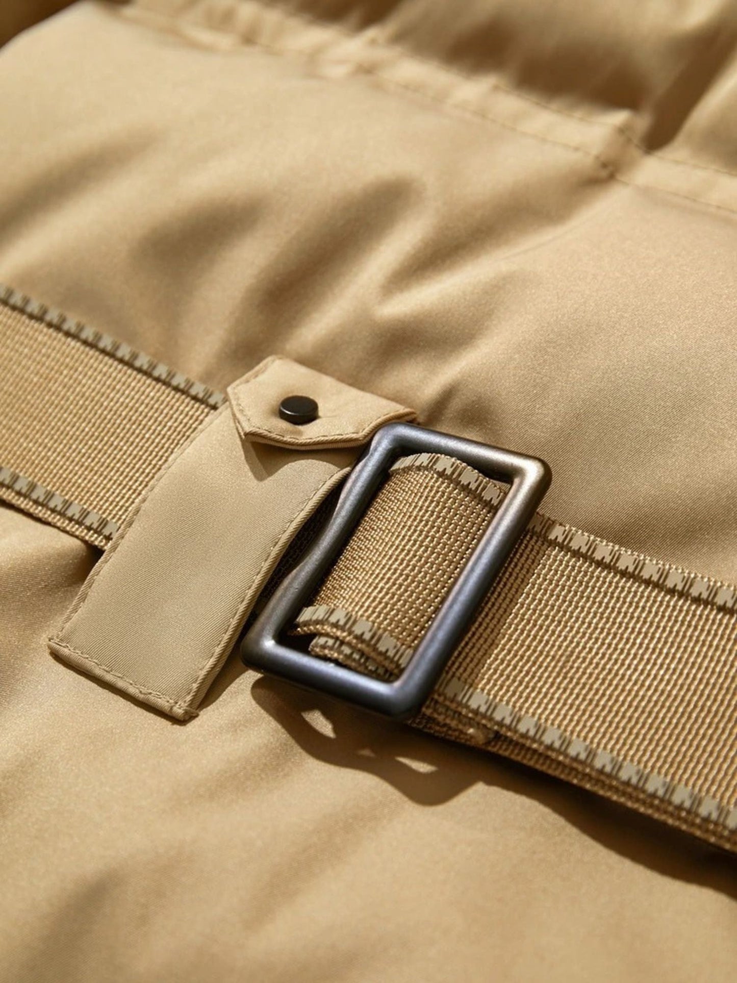 Extreme close-up of the belt buckle on the beige coat, showing textured fabric and metal hardware in detail