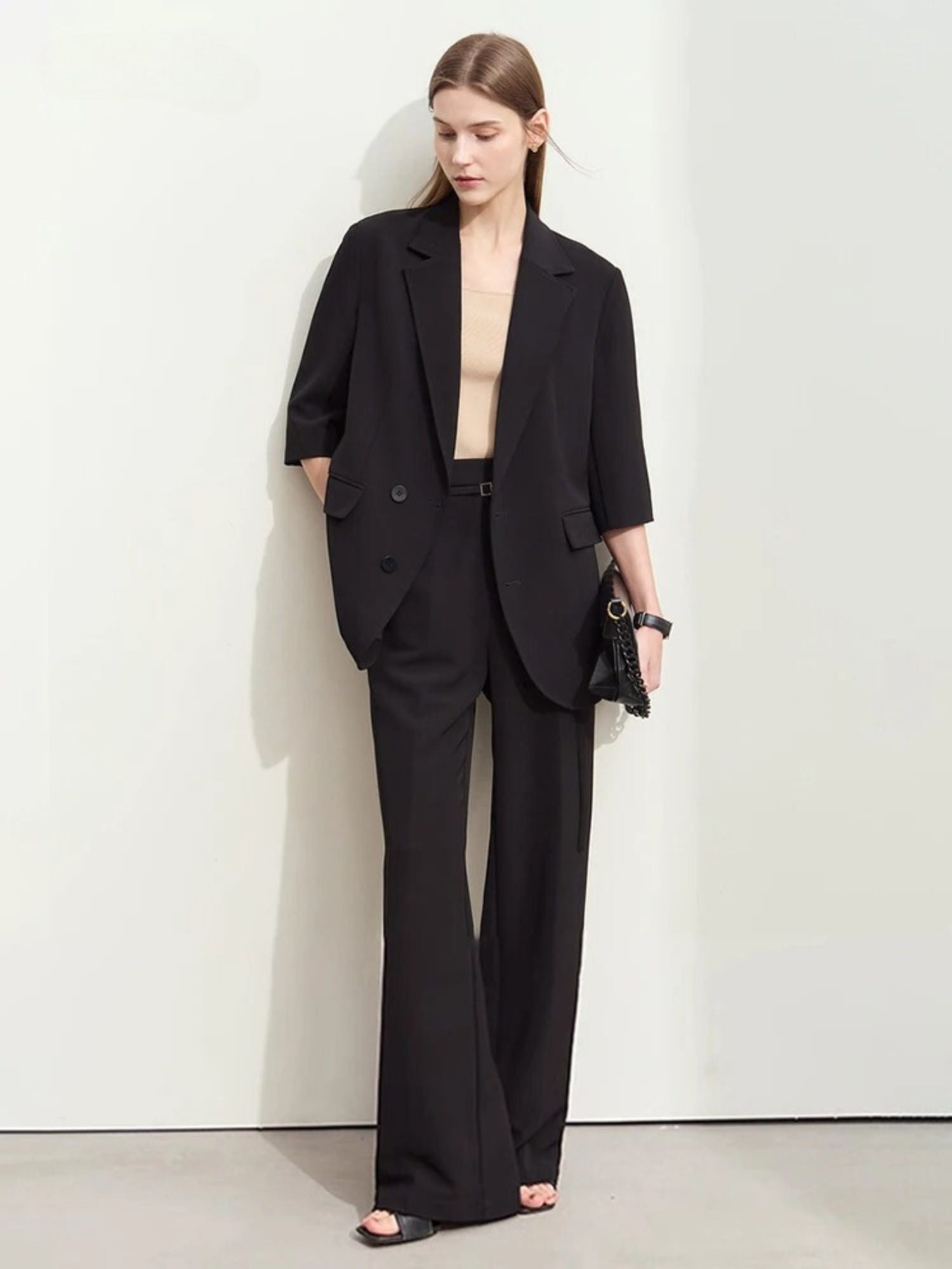Woman in a black oversized blazer with elbow-length sleeves and matching wide-leg trousers, paired with a beige top and black clutch