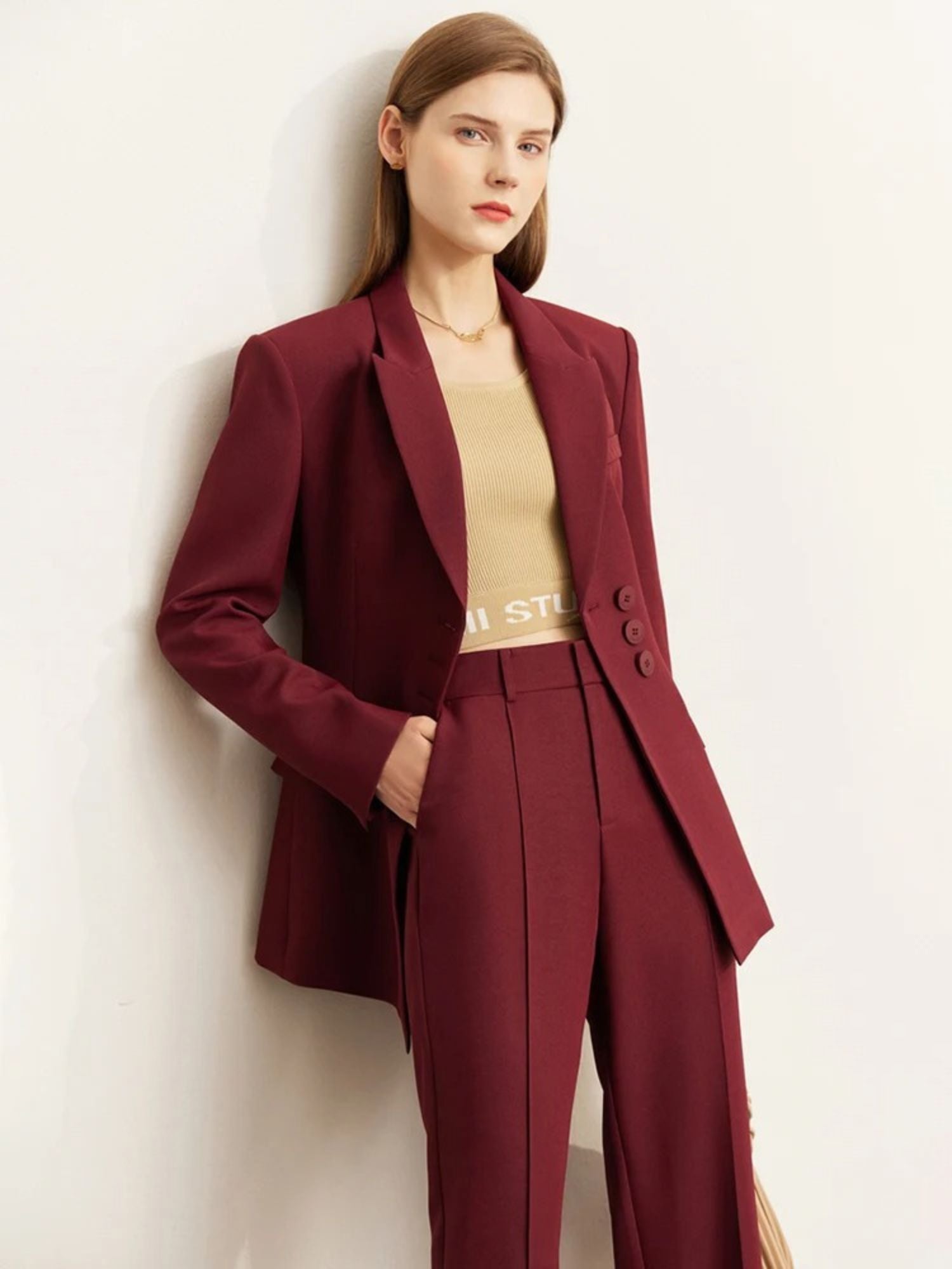 Woman in a burgundy pantsuit with a beige top underneath, holding one side of the blazer