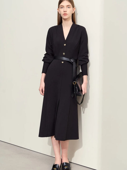 Women's black midi dress with V-neckline, long sleeves, button-front closure, and belted waist. Model wearing black loafers and carrying a black handbag