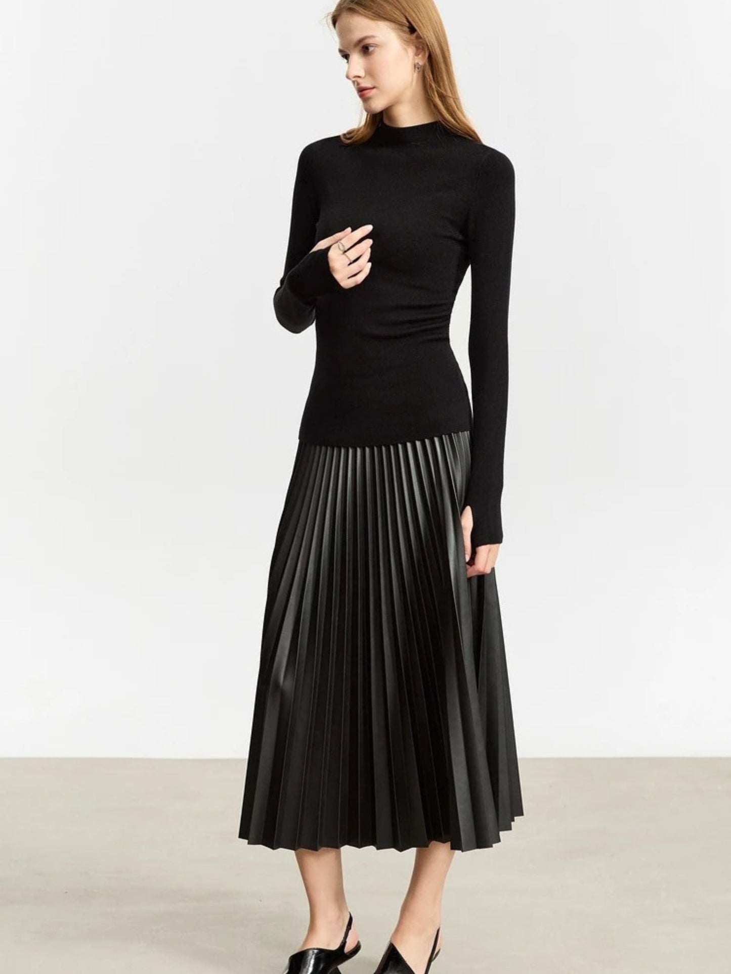 Front view of black faux leather pleated midi skirt paired with black long-sleeve top