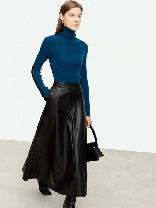Women's black faux leather midi skirt with A-line silhouette, styled with teal turtleneck and black boots. Model carrying black handbag
