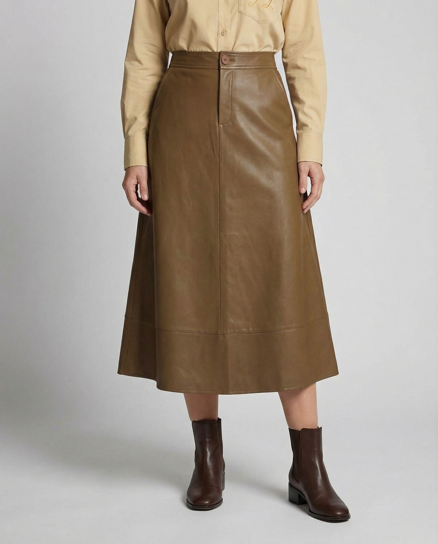 Person wearing a brown leather skirt with a beige shirt on a light gray background