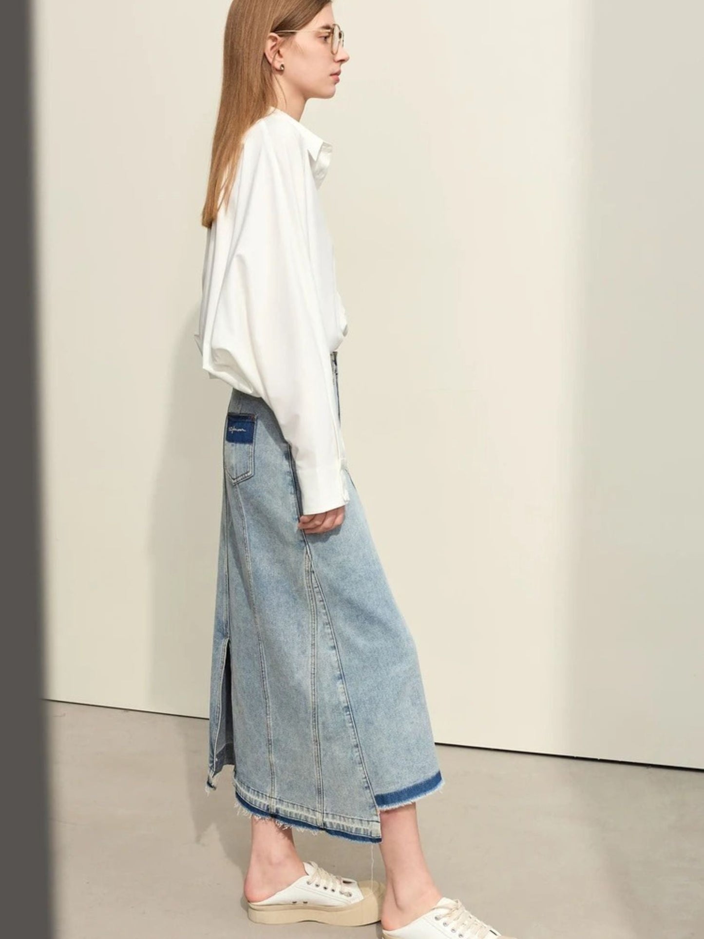 Side view of light blue denim skirt with front slit, paired with oversized white sweater and beige flats