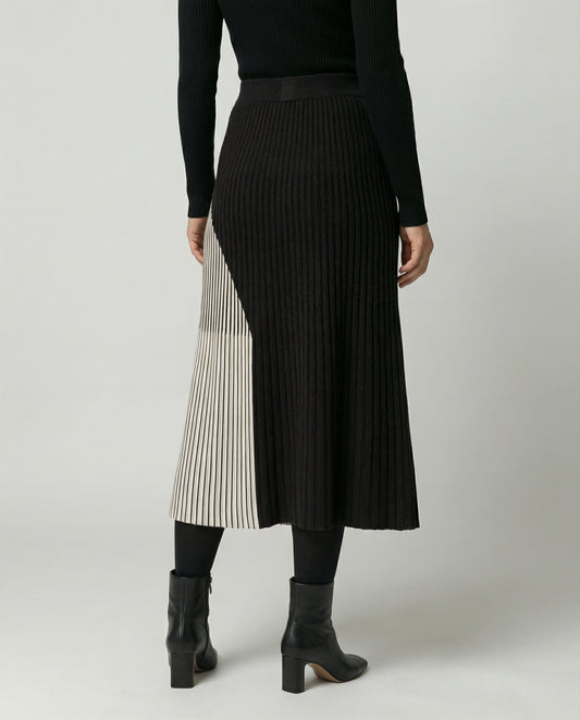 Person wearing a black ribbed skirt with a white pleated panel on a plain background