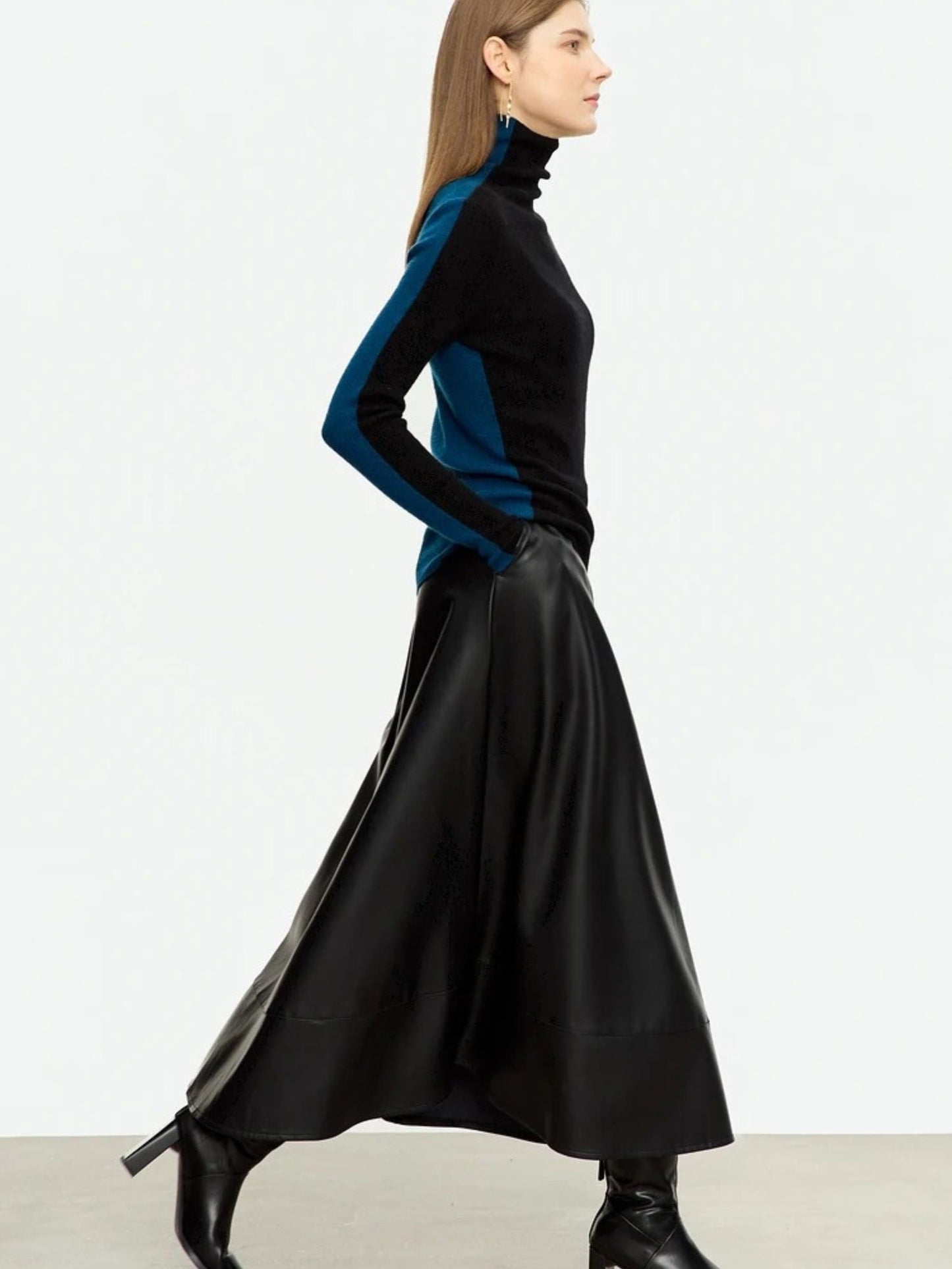 Side view of black faux leather midi skirt with A-line shape, worn with teal turtleneck and black boots