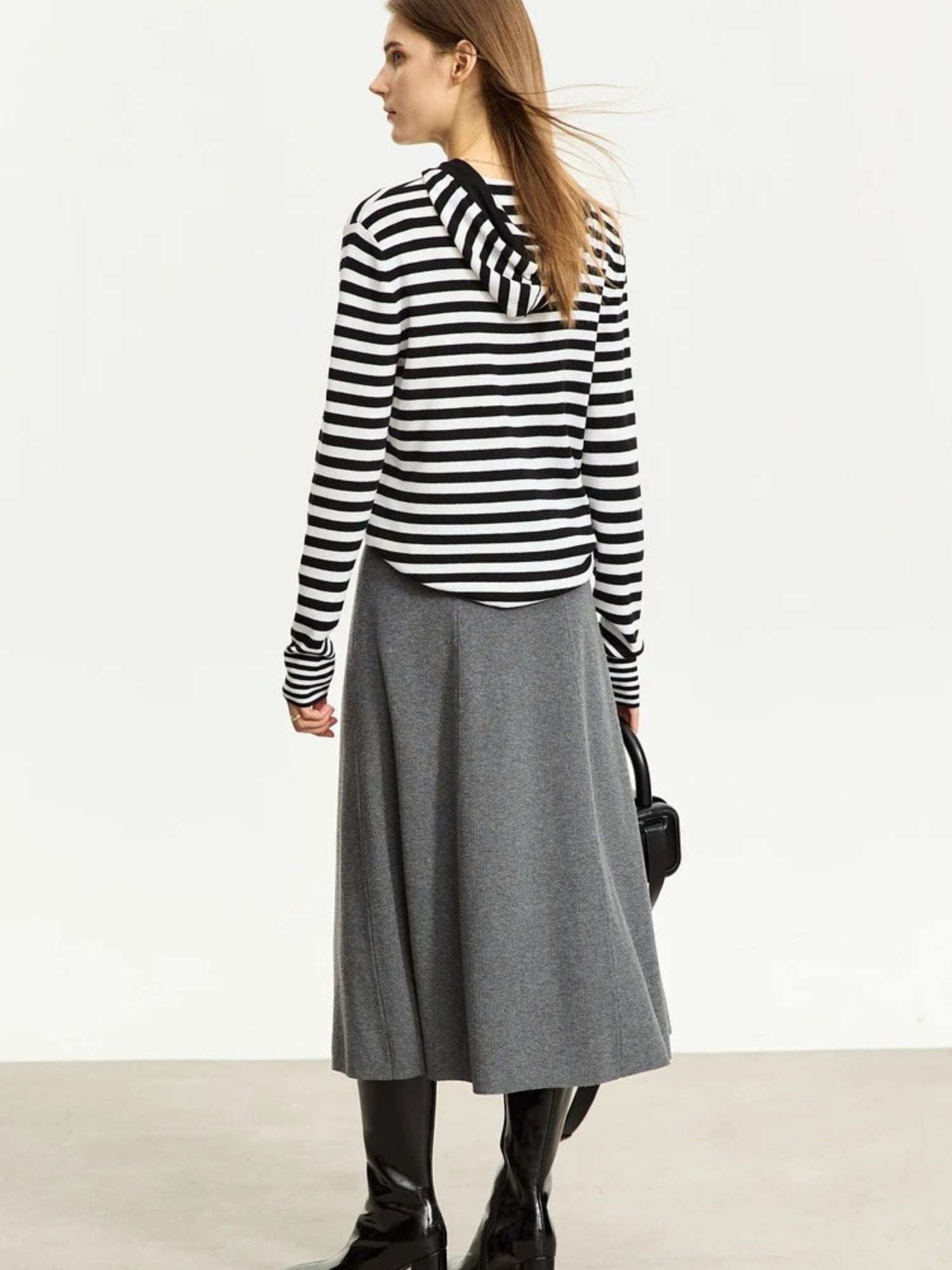 Woman wearing a black and white striped sweater and gray skirt on a plain background