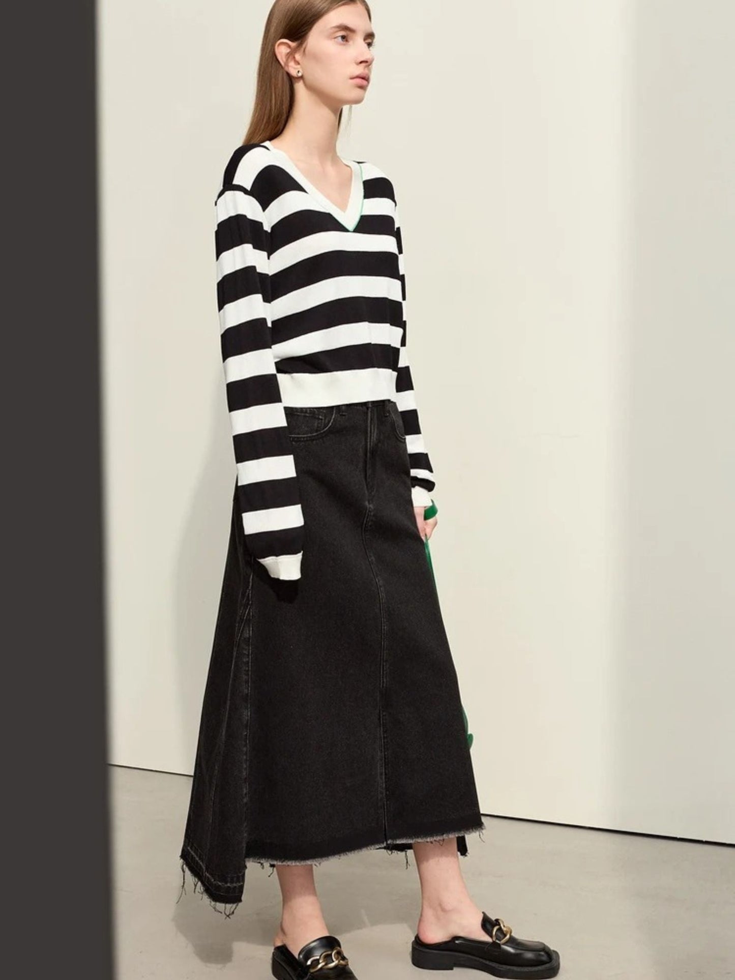 Rear view of black denim midi skirt styled with striped sweater and flat shoes. Clean A-line silhouette