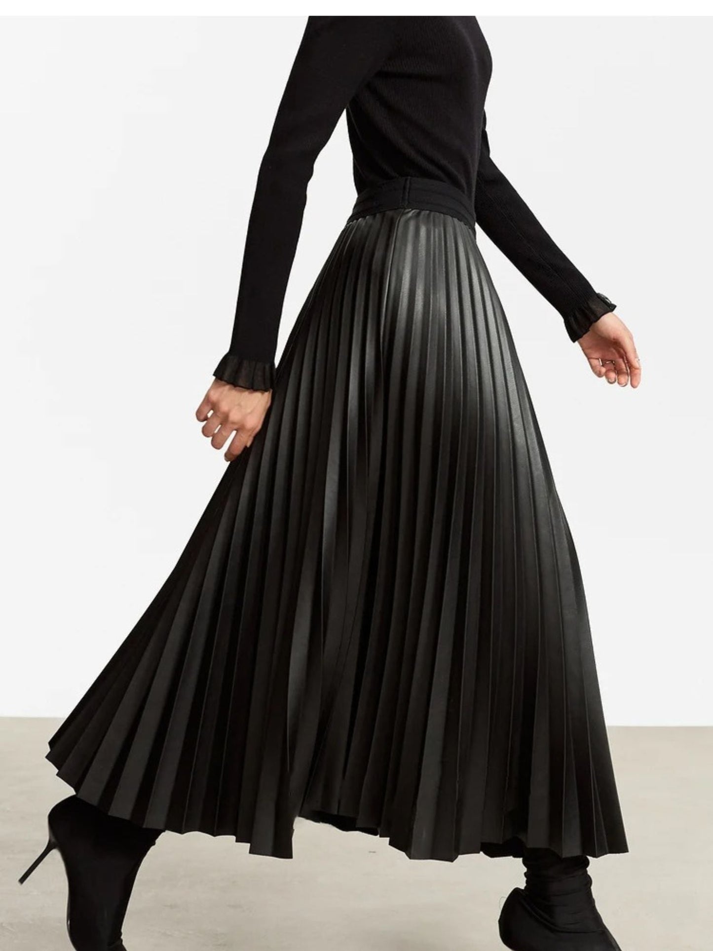 Walking side view of black faux leather pleated midi skirt showcasing flow and movement