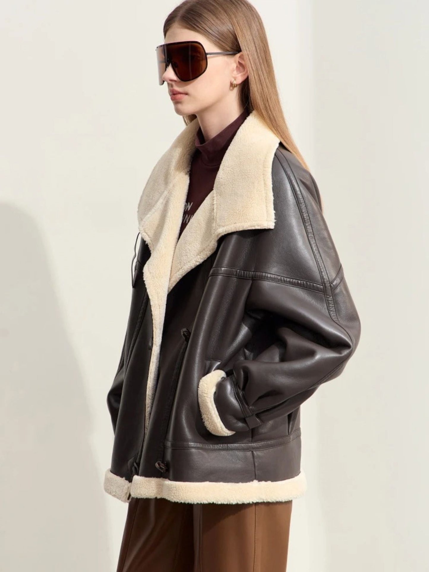 Three-quarter angle view of the model standing with hands in pockets, giving a full look at the jacket’s front design, zippers, and oversized lapel