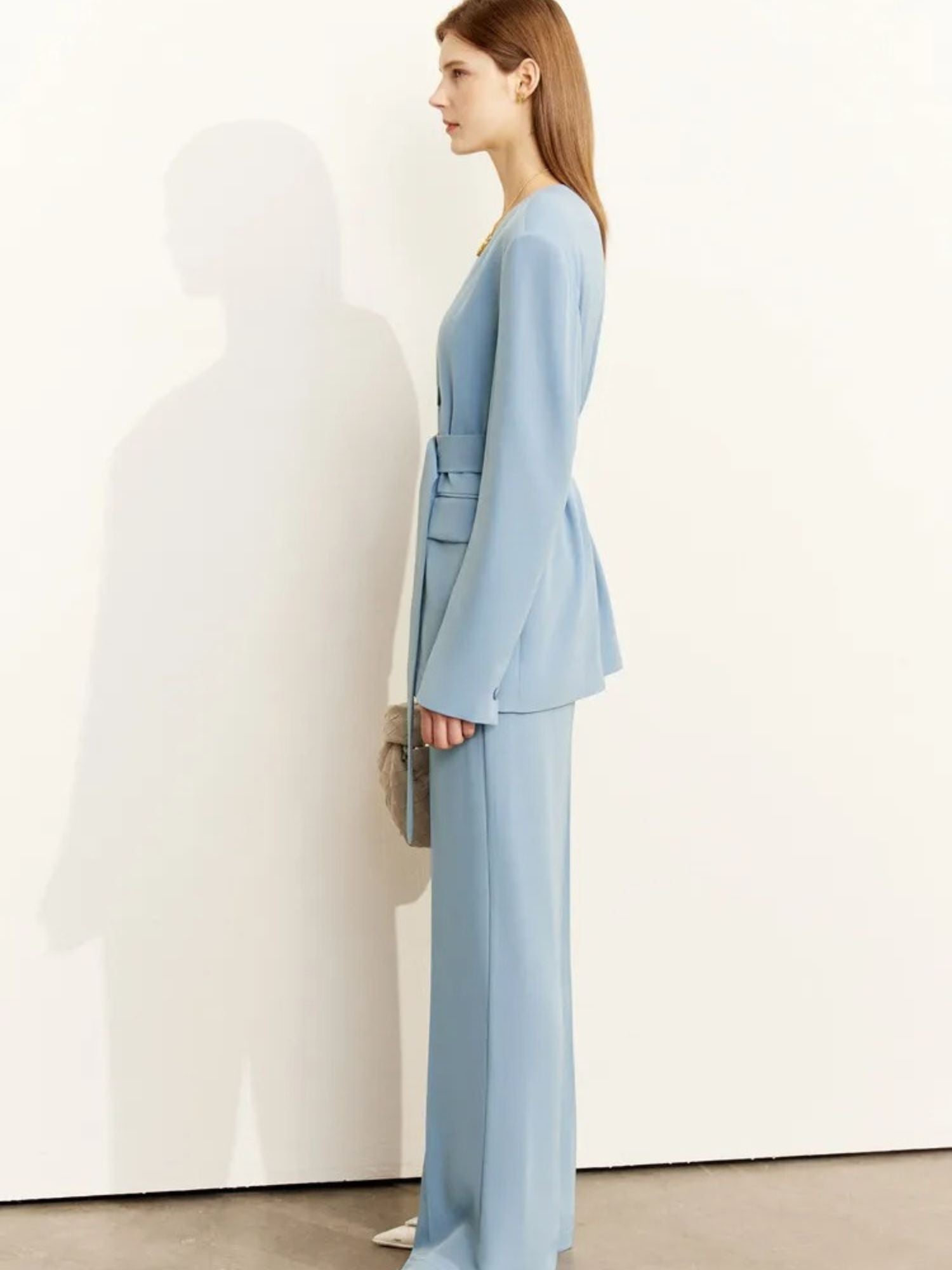 Woman wearing a light blue suit standing against a white wall