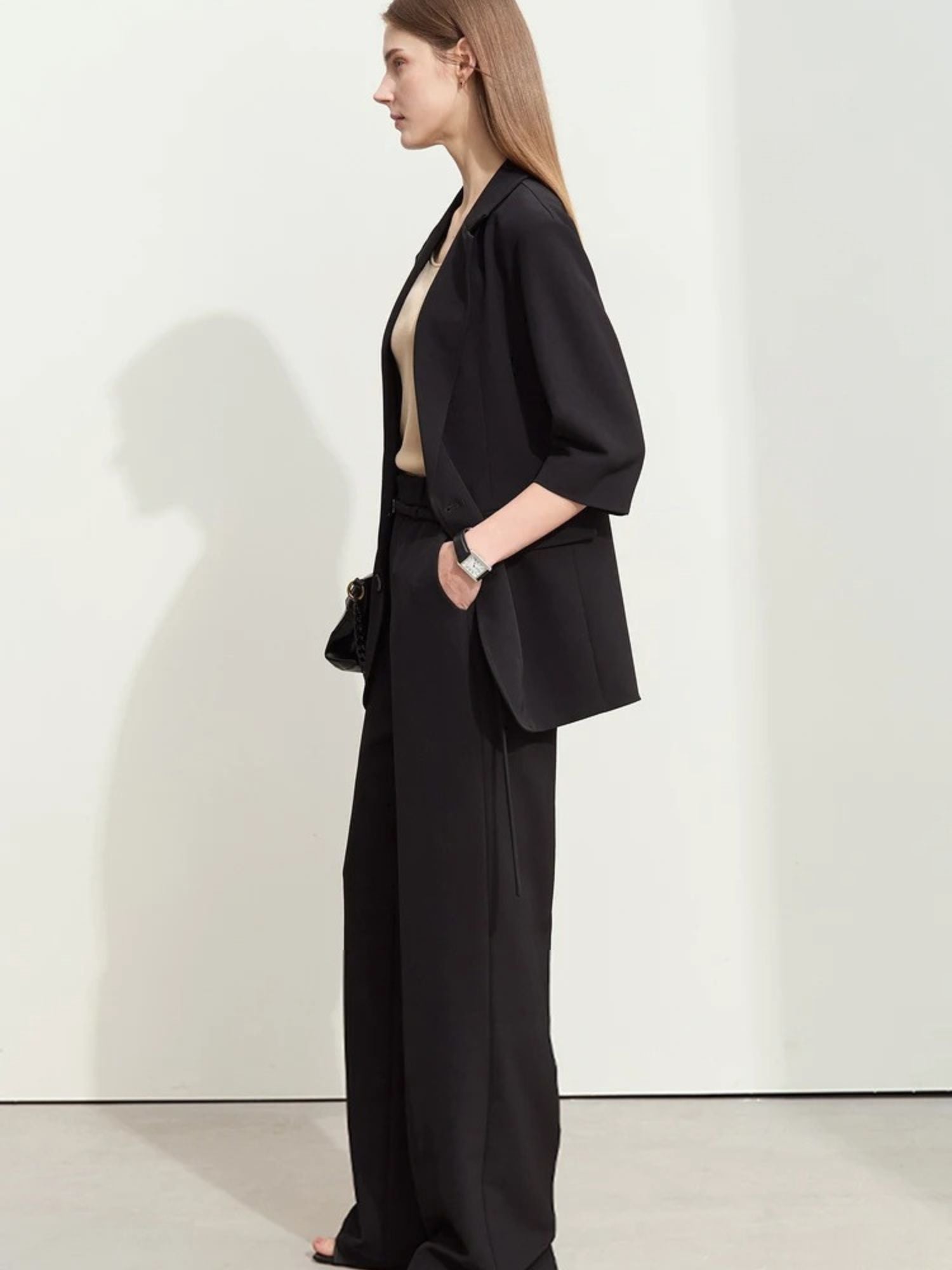 Three-quarter side view of woman in black pantsuit with open blazer and nude top
