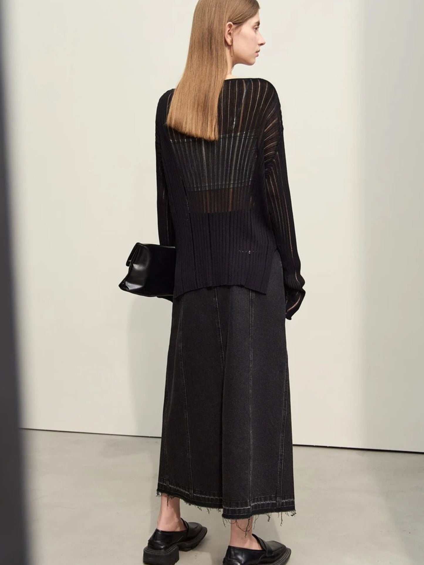 Full body back pose of black denim midi skirt styled with loose black top. Minimalist, monochrome look