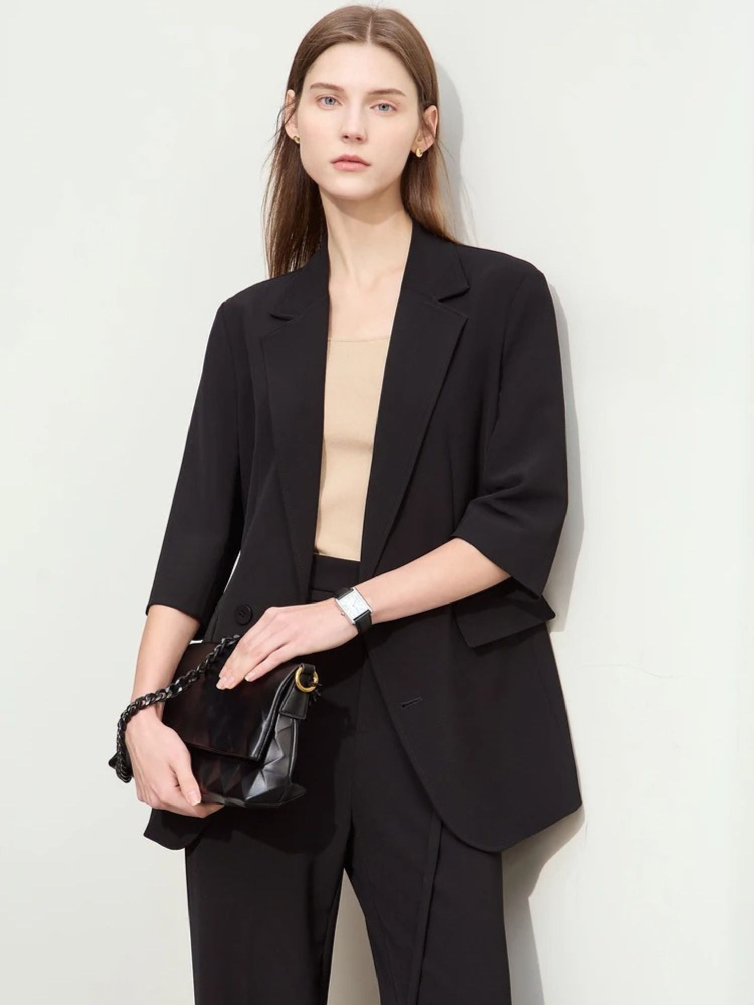 Close-up front view of woman in black elbow-length blazer and matching trousers with black accessories