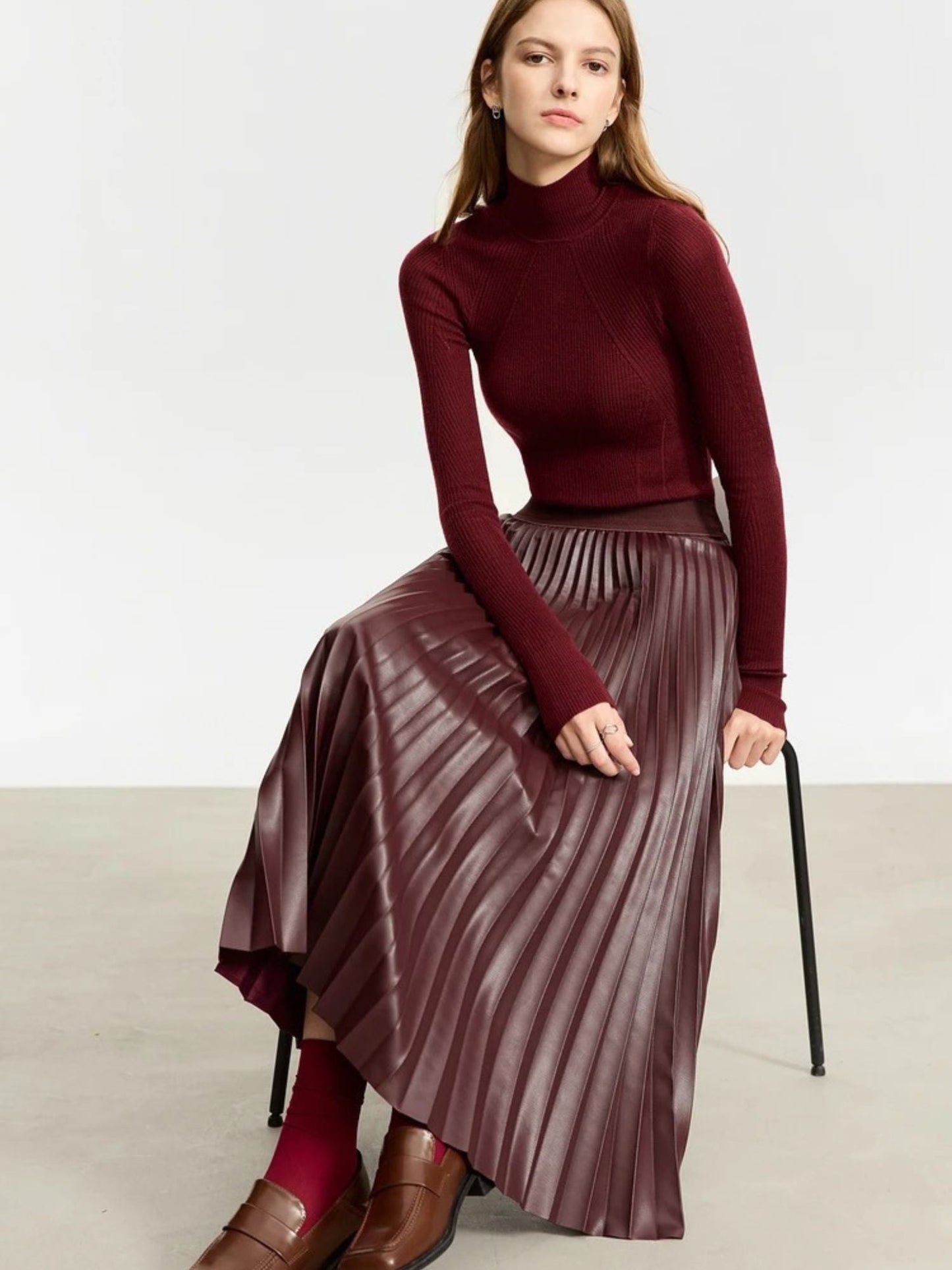 Seated front view of burgundy faux leather pleated midi skirt paired with matching burgundy top