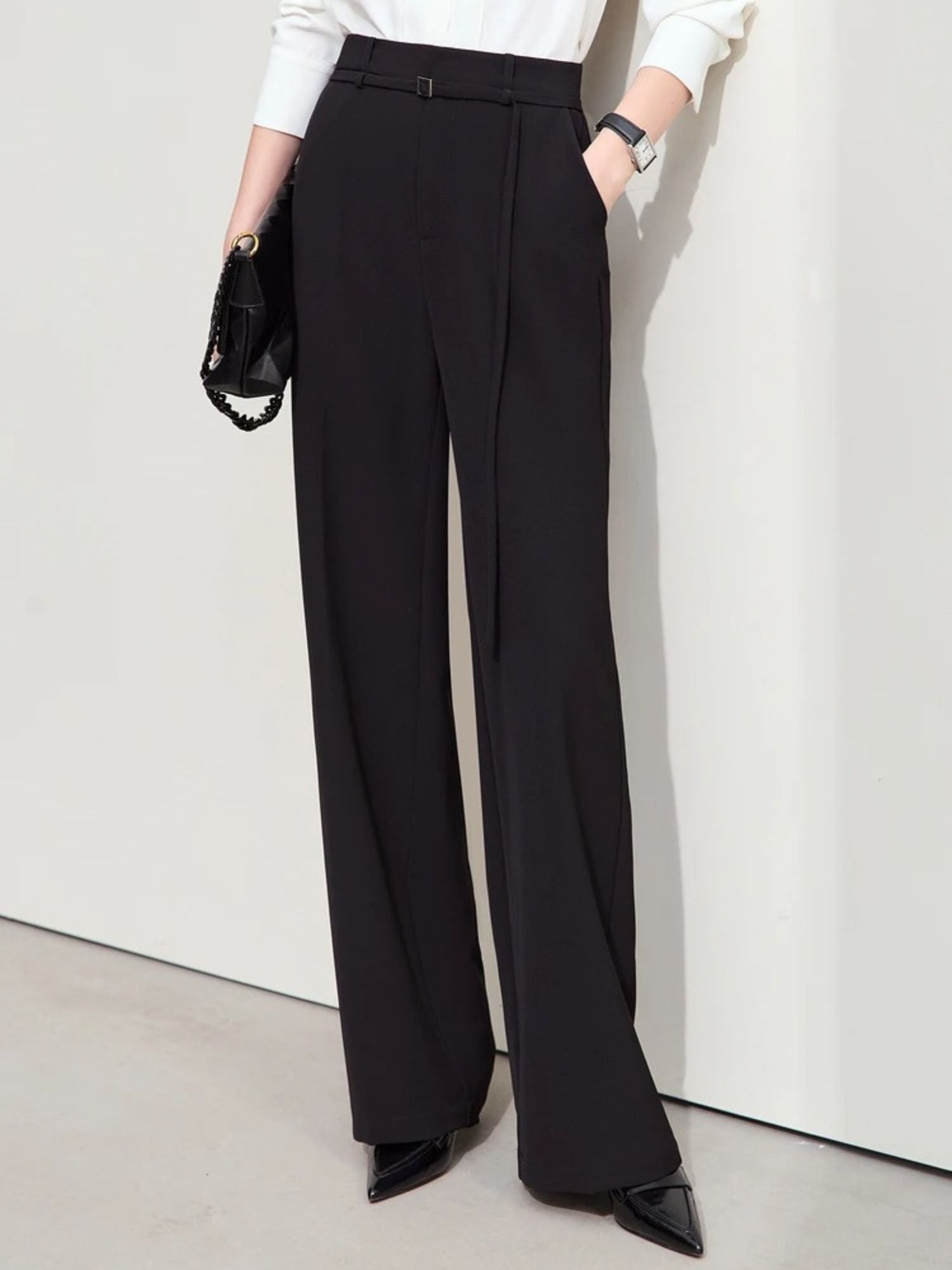 Side view of black wide-leg trousers worn with black heels, shown with white top and black clutch