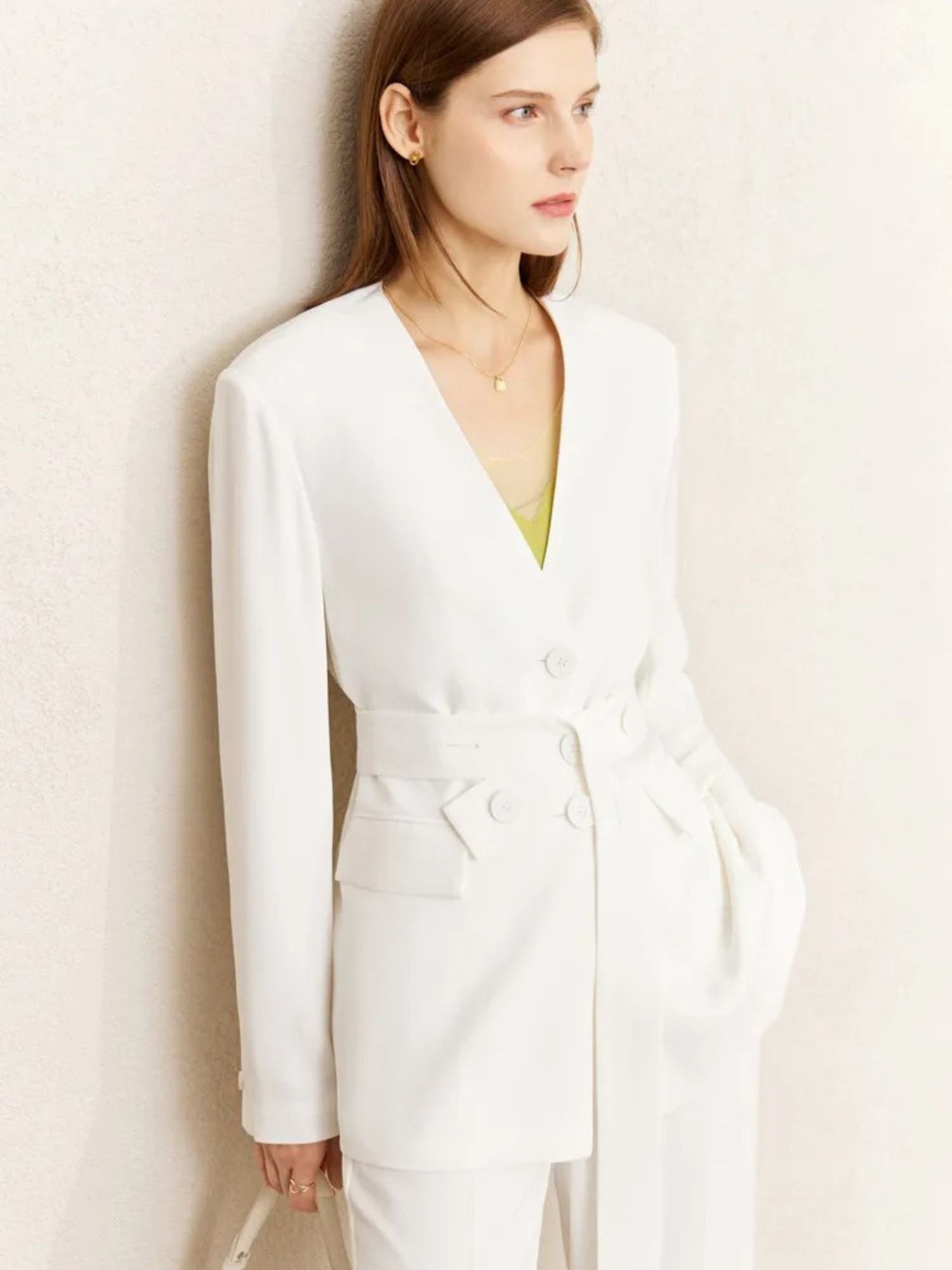 Close-up of woman wearing an all-white belted blazer and trousers with a hint of a yellow inner top