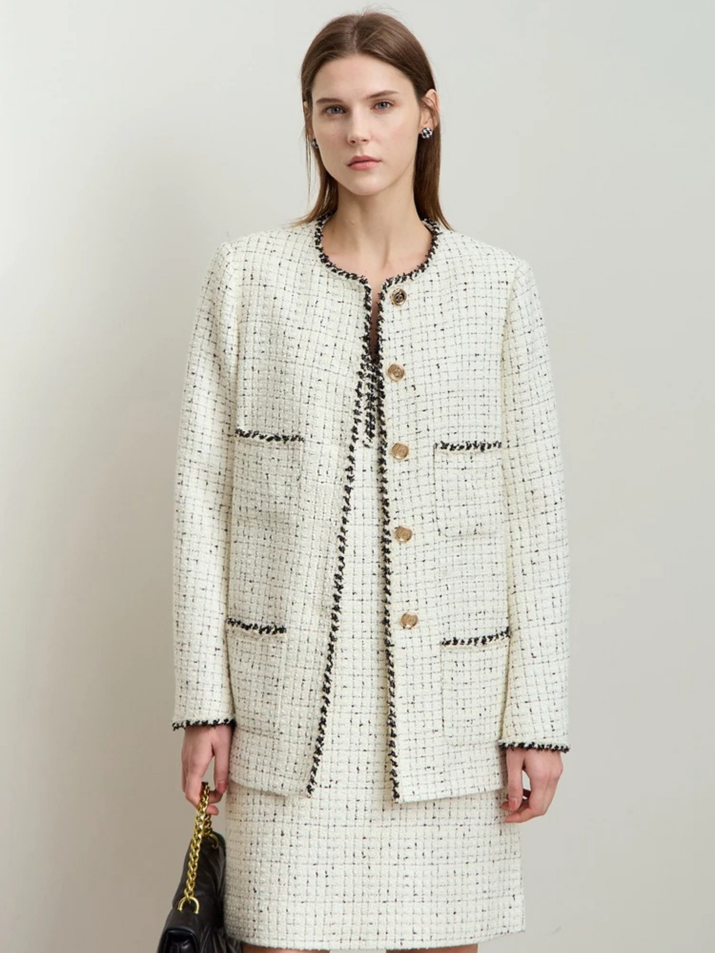 Front view of the cream tweed jacket and skirt on the same model. She has a neutral expression and is carrying a black bag