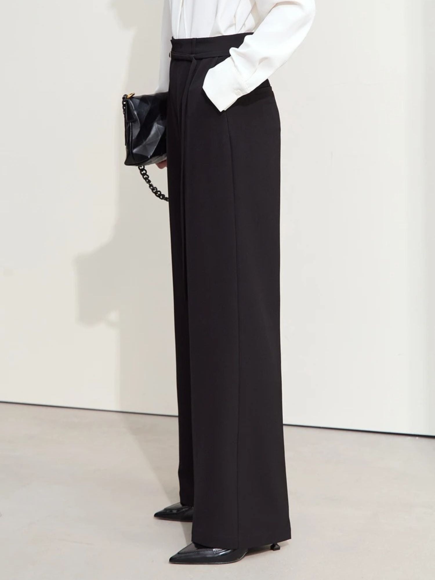 Angled back view of black wide-leg trousers styled with black heels and a white top