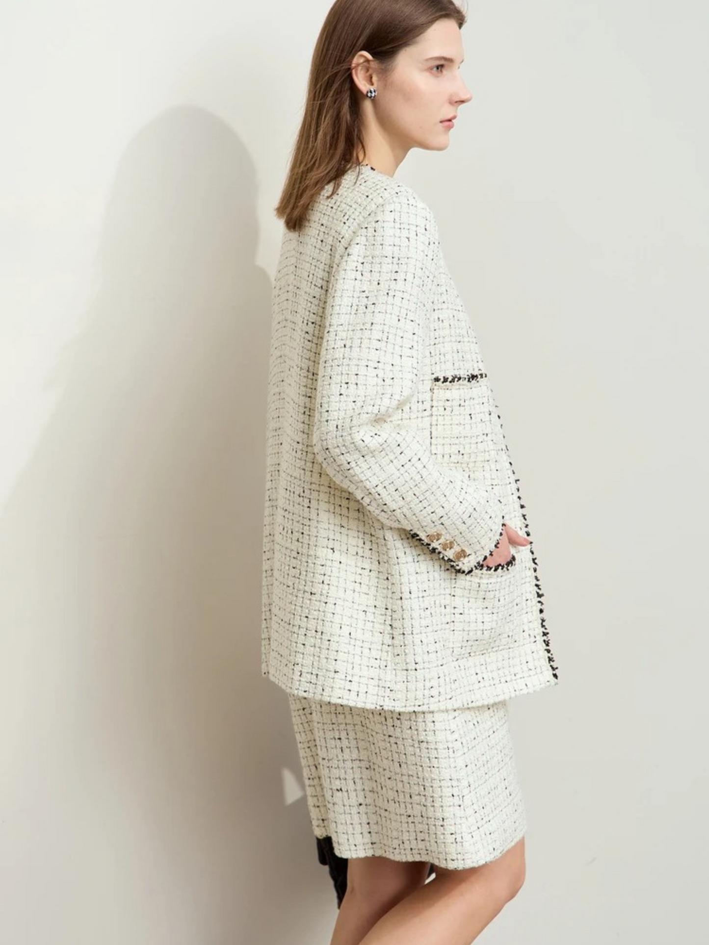 Side-back angle of the cream tweed outfit, showing the silhouette of the jacket from a different perspective. The lighting highlights the fabric texture