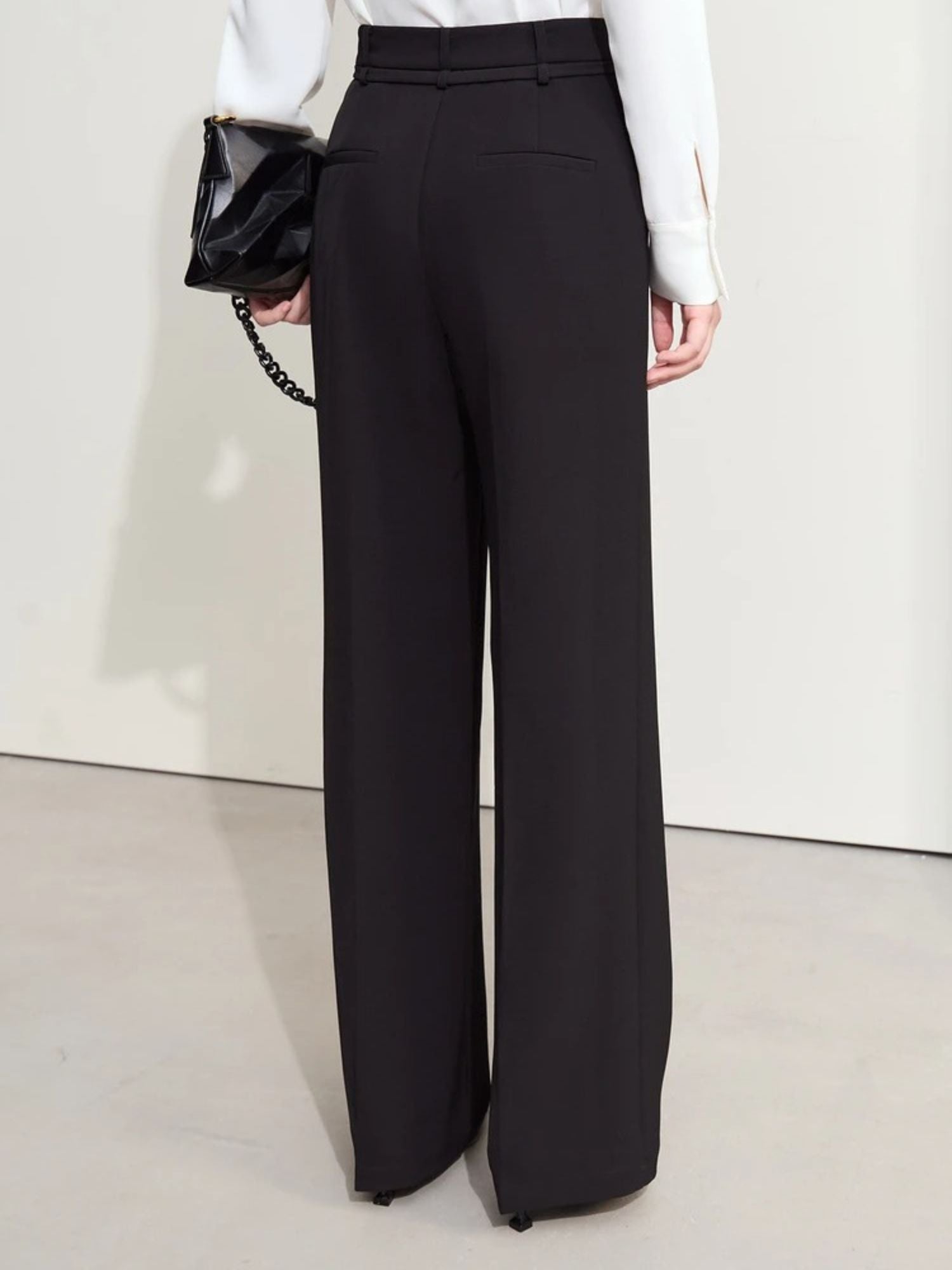 Back view of black trousers paired with black clutch and heels, white blouse partially visible