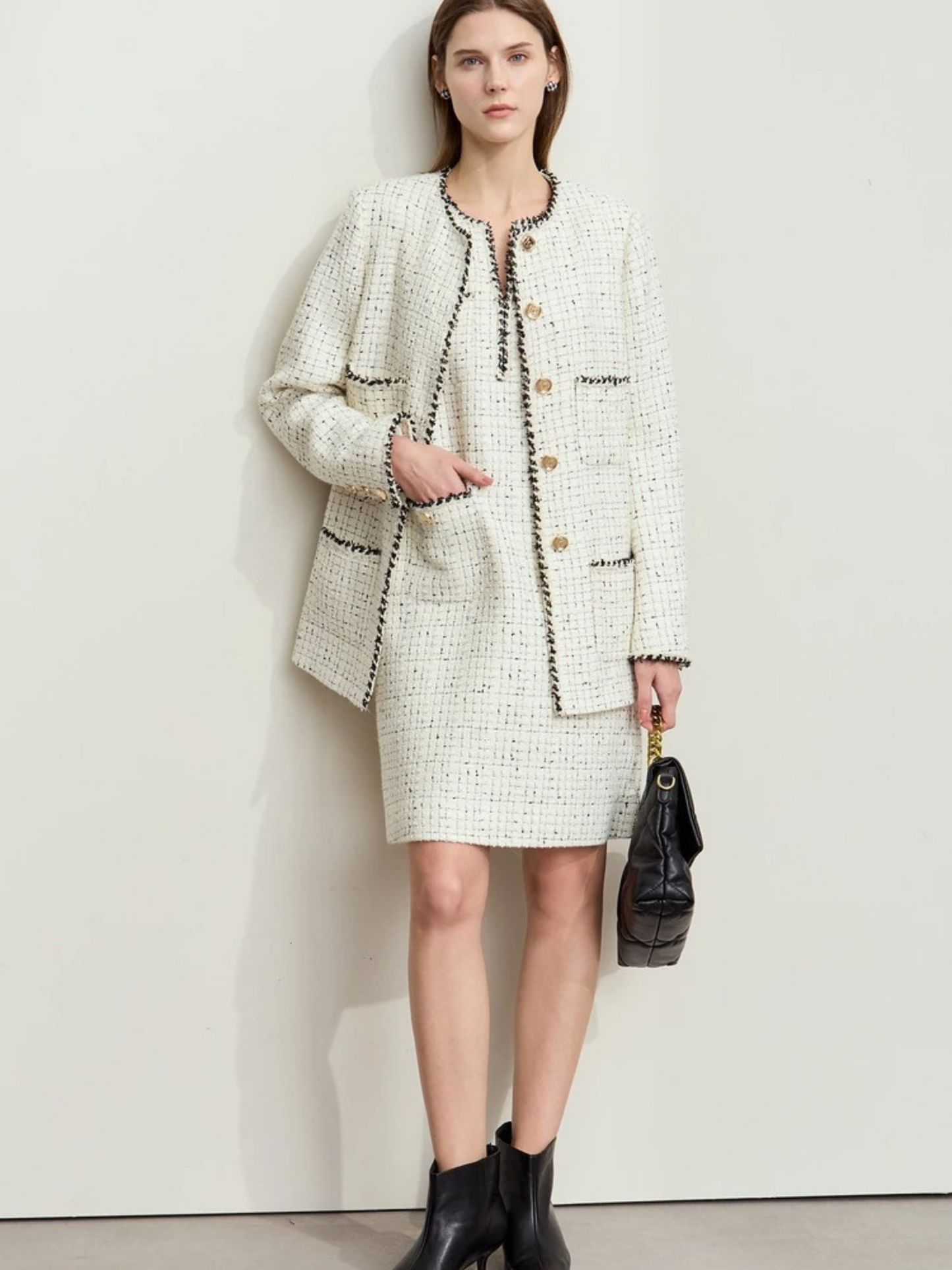 Model wearing cream tweed. She stands with her legs crossed, holding a black bag. The cream version has similar gold buttons and textured details