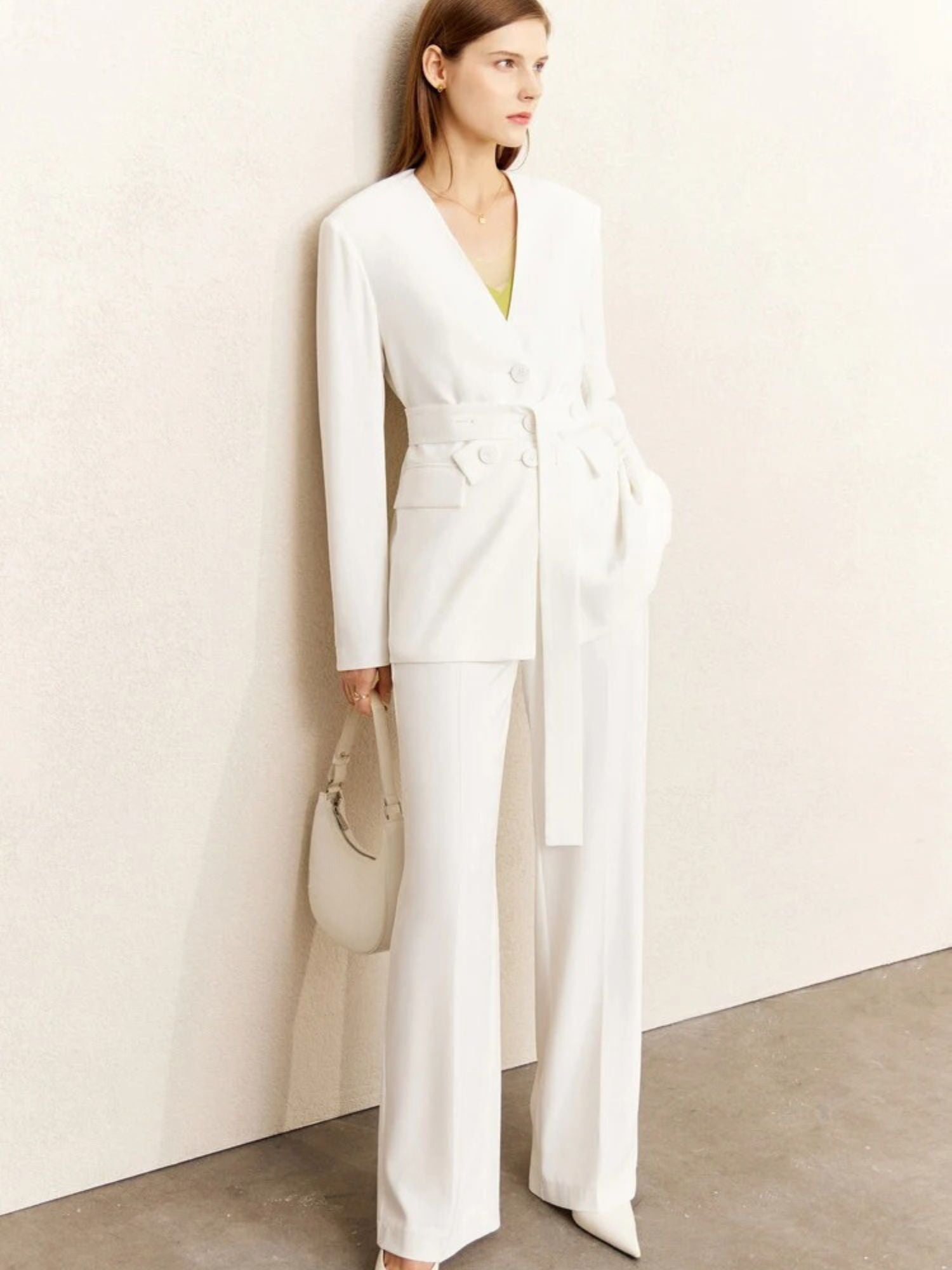 Woman standing in an all-white belted blazer and trousers set, slightly angled pose