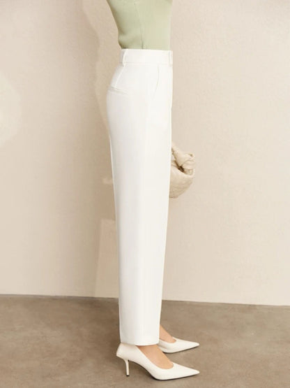 Close-up side view of high-waisted white trousers with tucked-in green top and beige handbag
