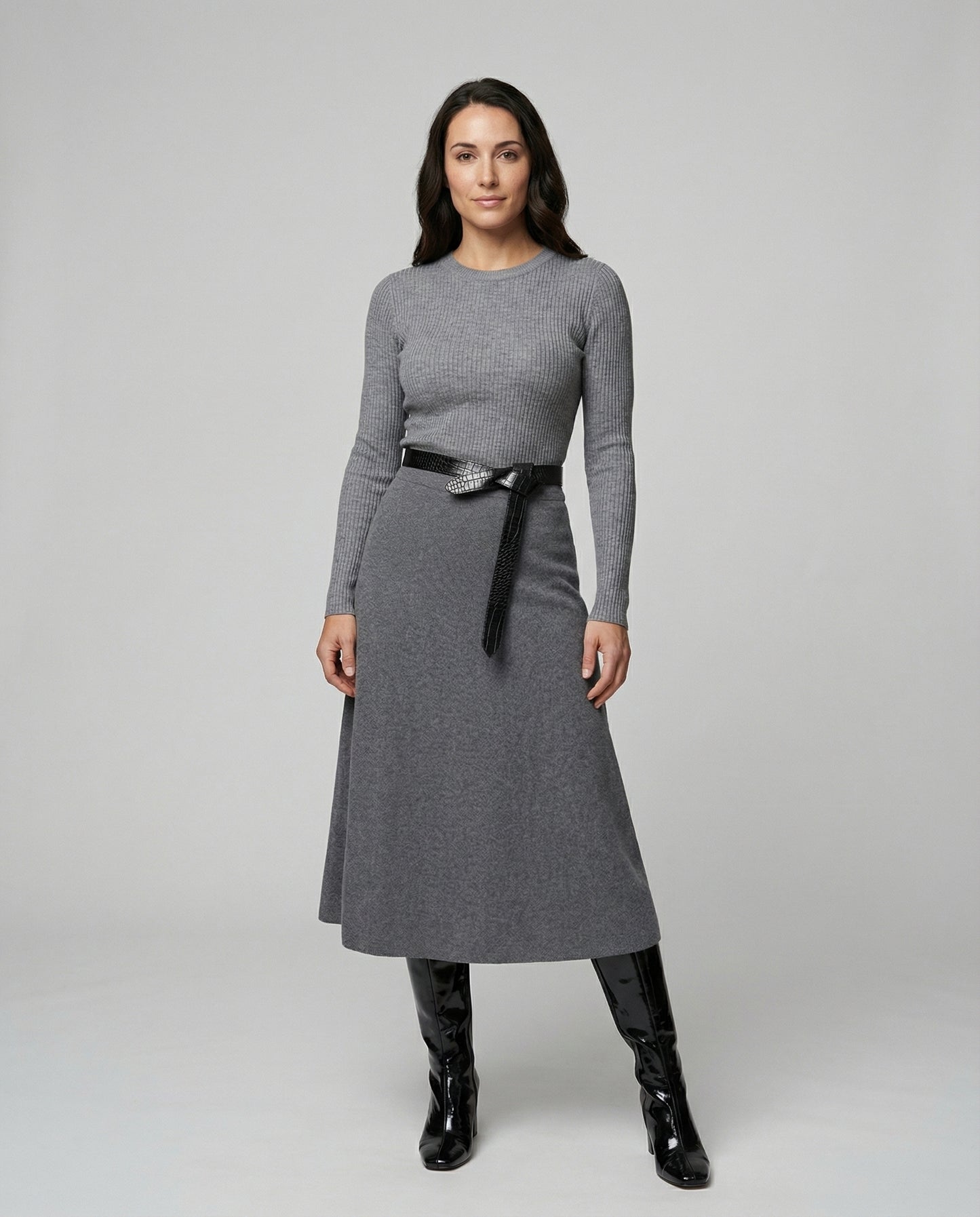 Woman wearing a gray dress with a black belt and black boots on a white background