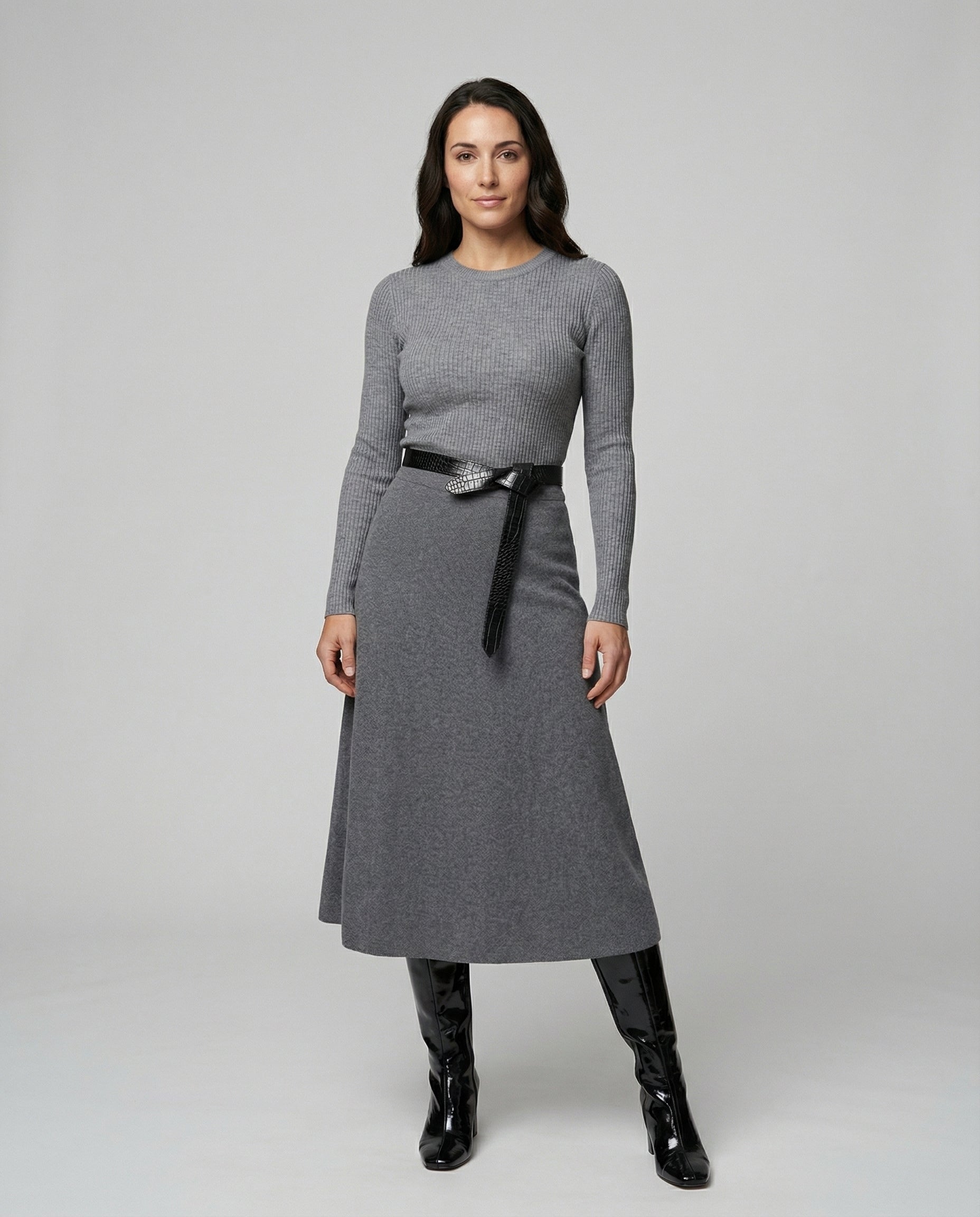 Woman wearing a gray dress with a black belt and black boots on a white background