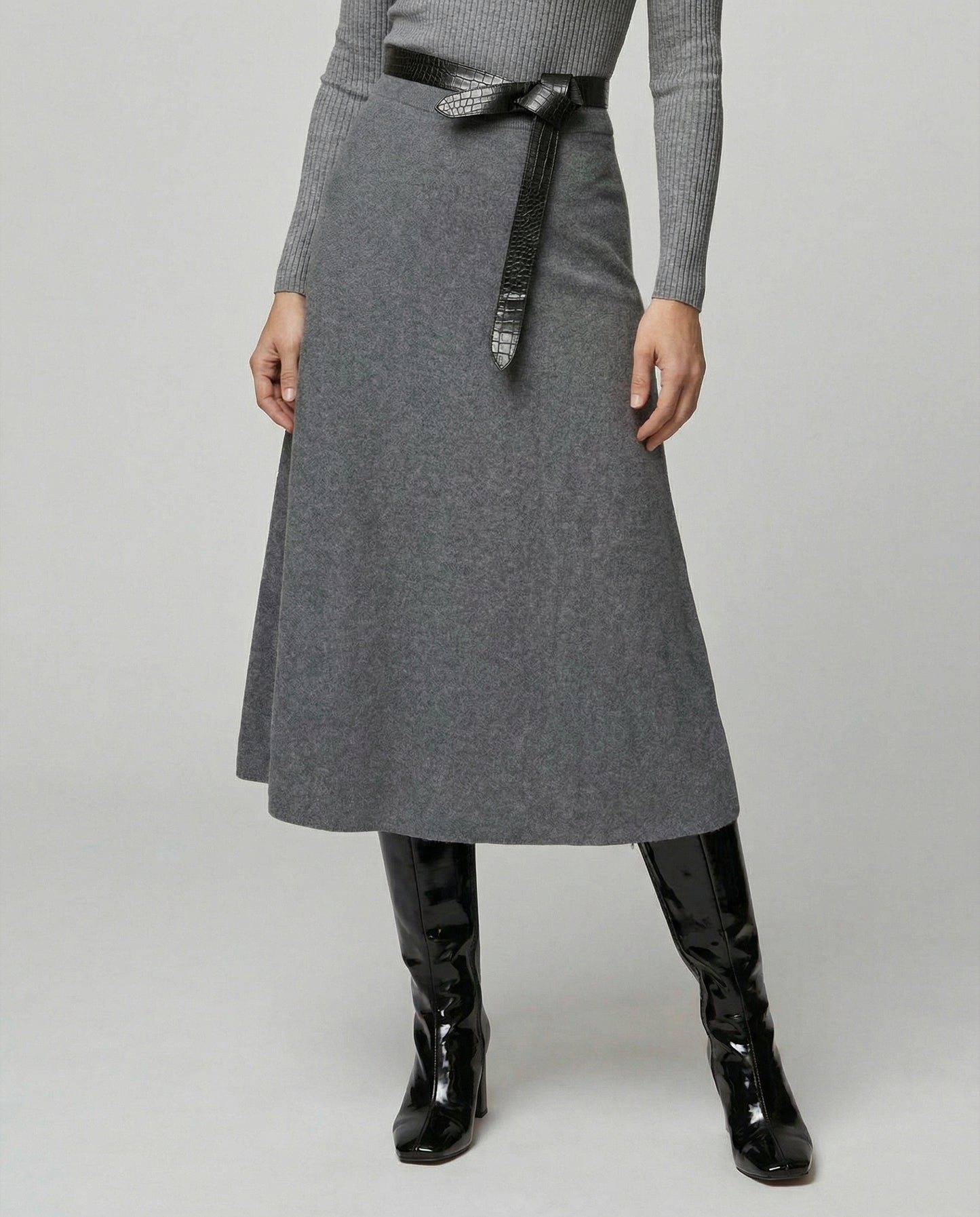 Person wearing a gray skirt with a black belt and black boots on a light gray background