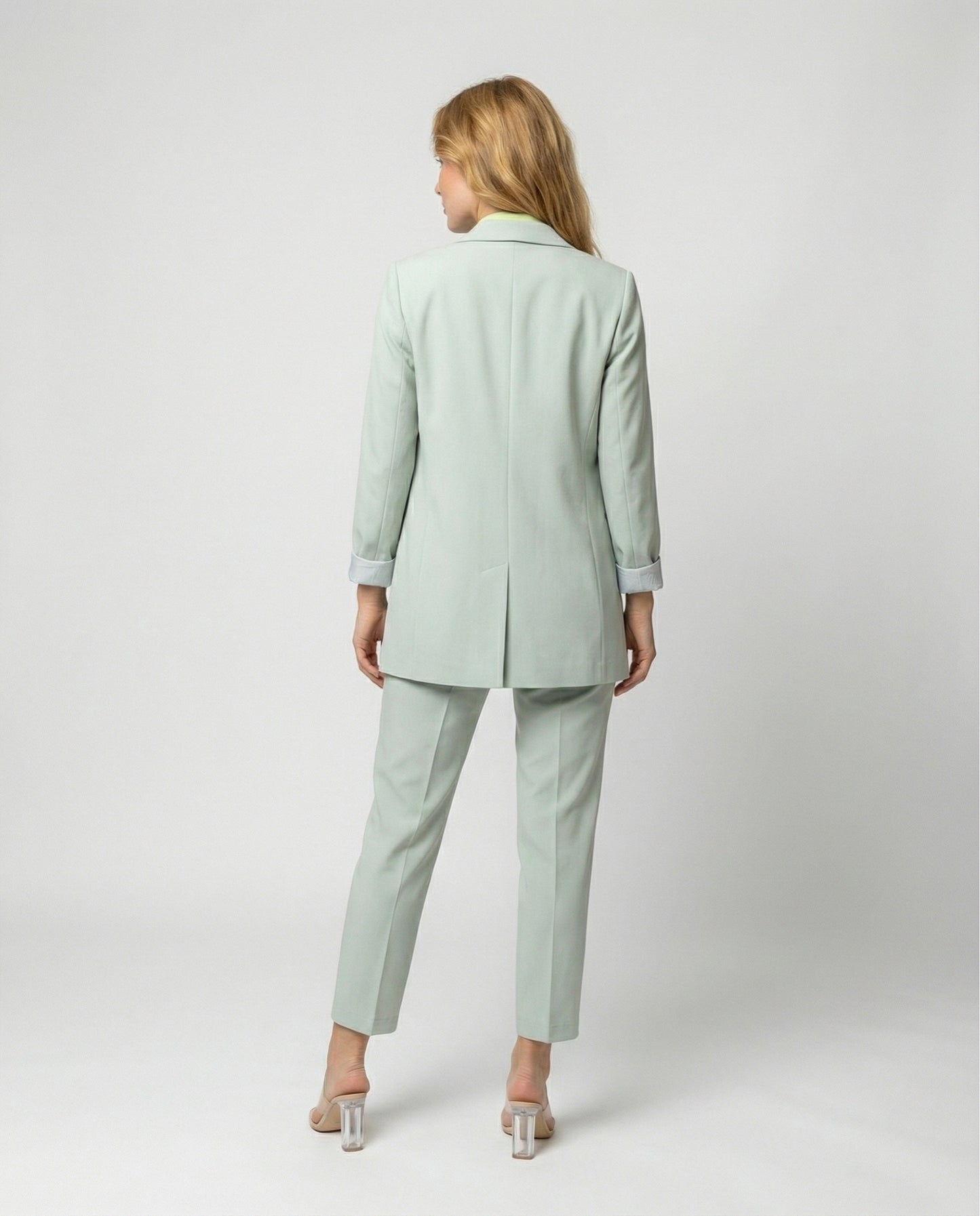 Woman wearing a light green suit standing against a white background