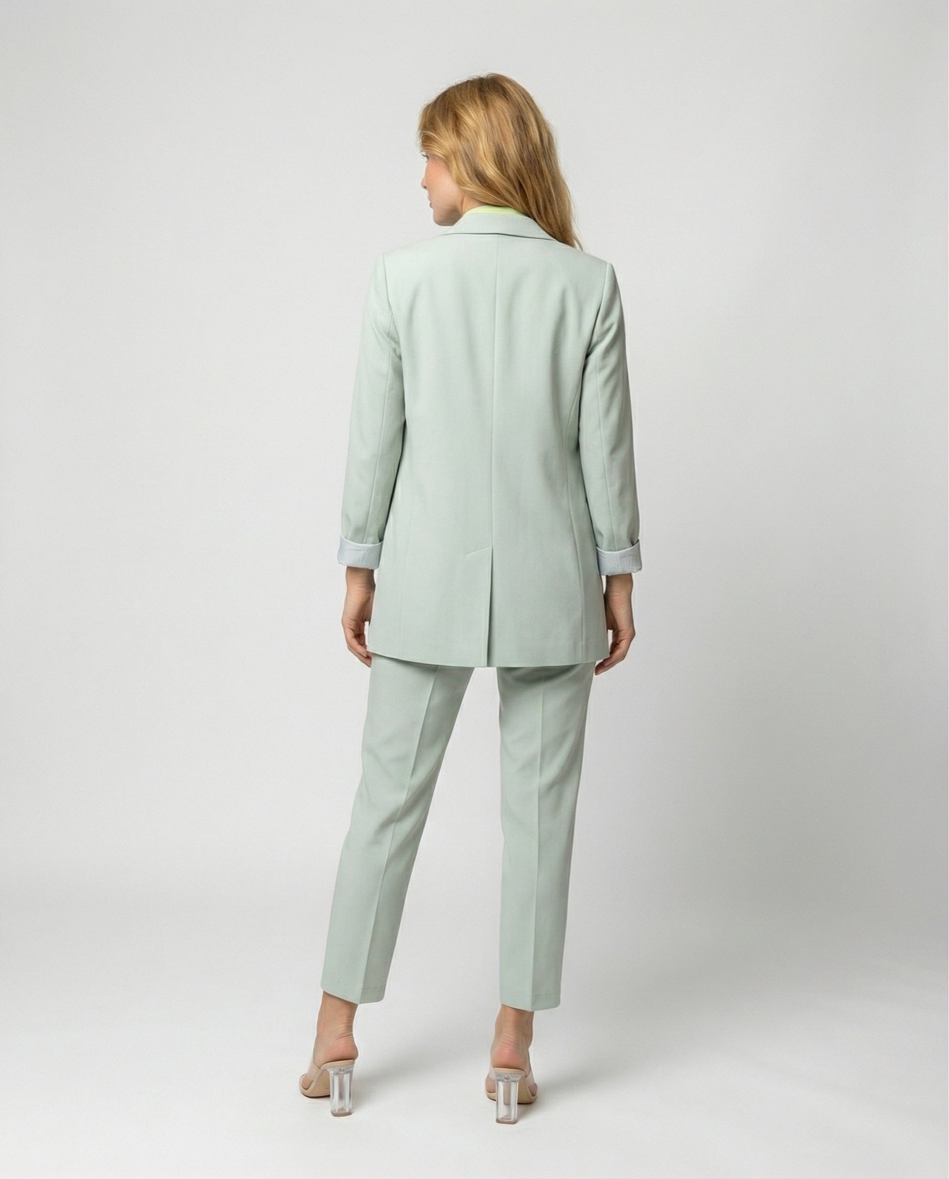 Woman wearing a light green suit standing against a white background