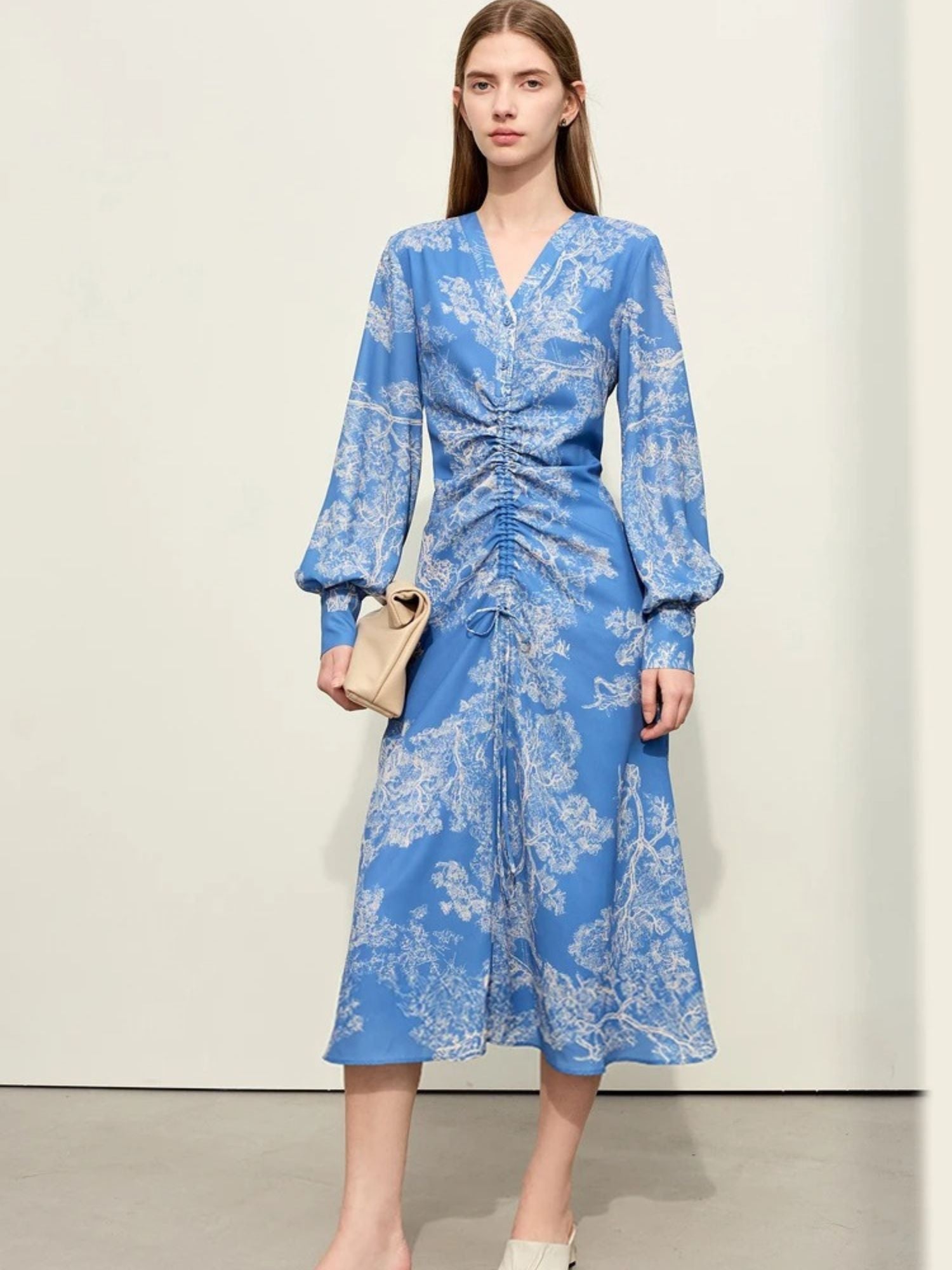 Women's blue long-sleeve wrap midi dress with white floral print, ruched front detail, and V-neckline. Model carrying beige handbag