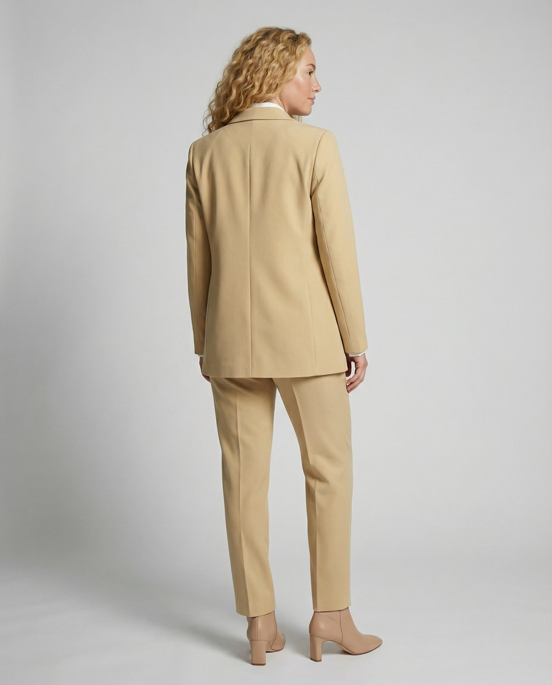 Woman wearing a beige suit standing against a plain background