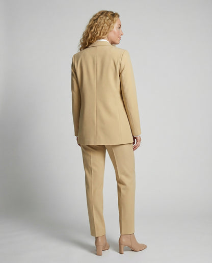 Woman wearing a beige suit standing against a plain background