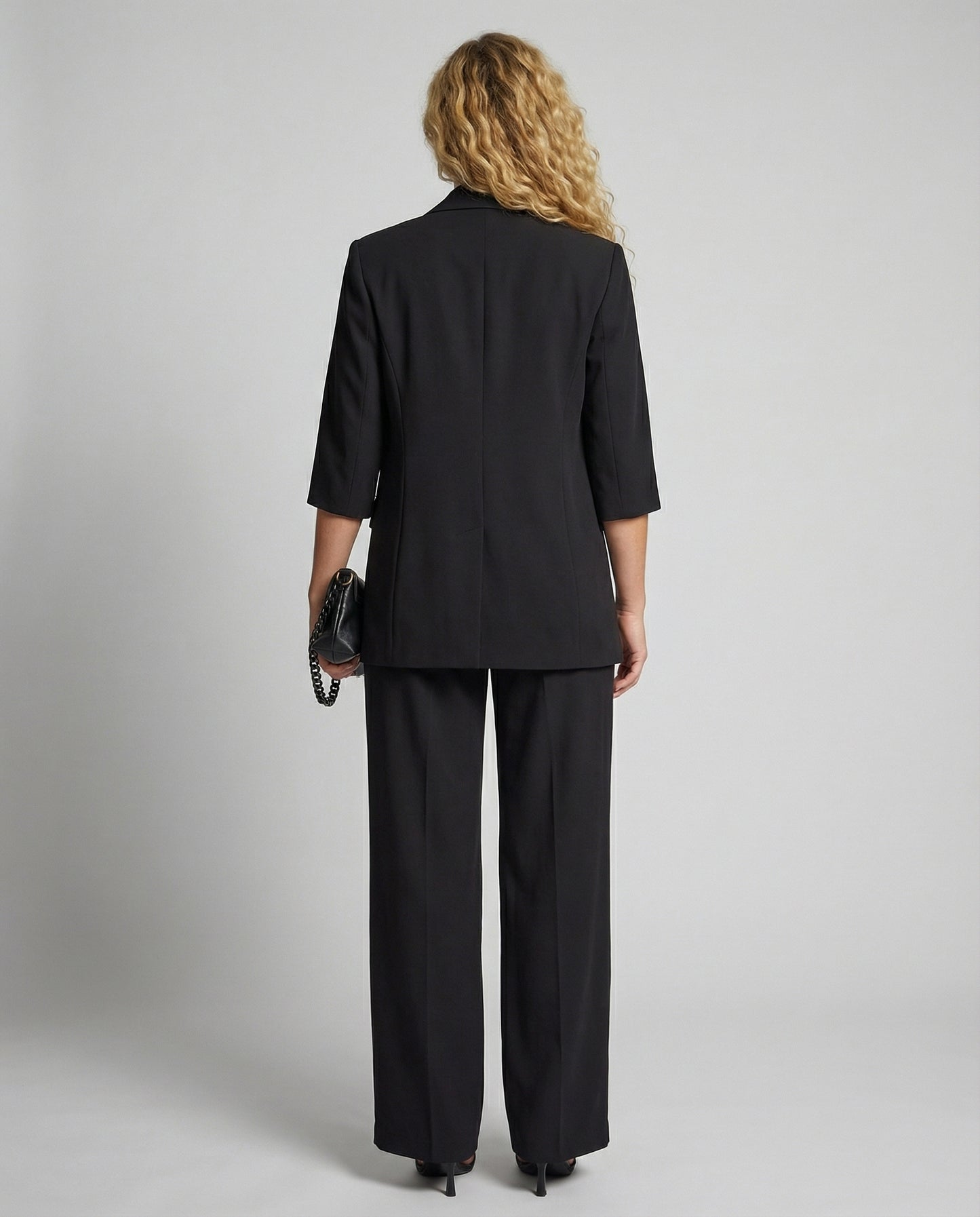 Person wearing a black suit standing against a plain background