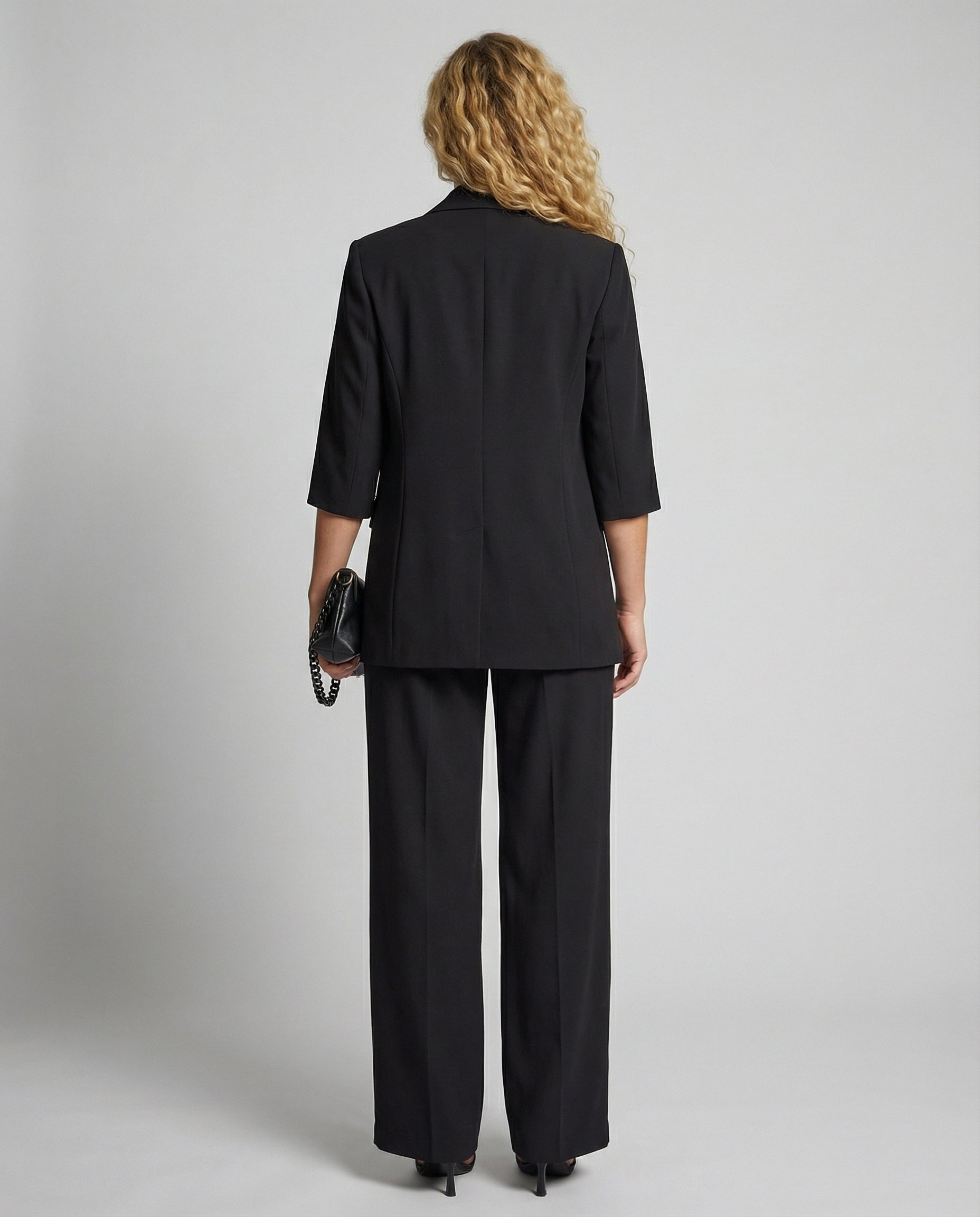 Person wearing a black suit standing against a plain background
