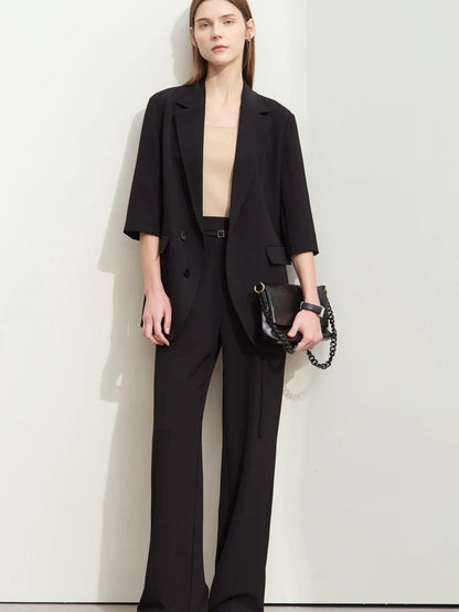 Front-facing woman in black wide-leg pants and elbow-sleeve blazer over a beige top, holding a black handbag