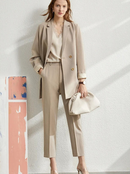 Full-body shot of woman in beige pantsuit and blouse, holding a white handbag