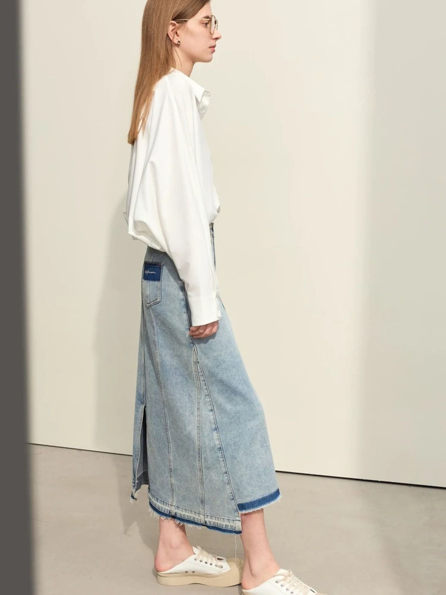Side view of light blue denim skirt with front slit, paired with oversized white sweater and beige flats