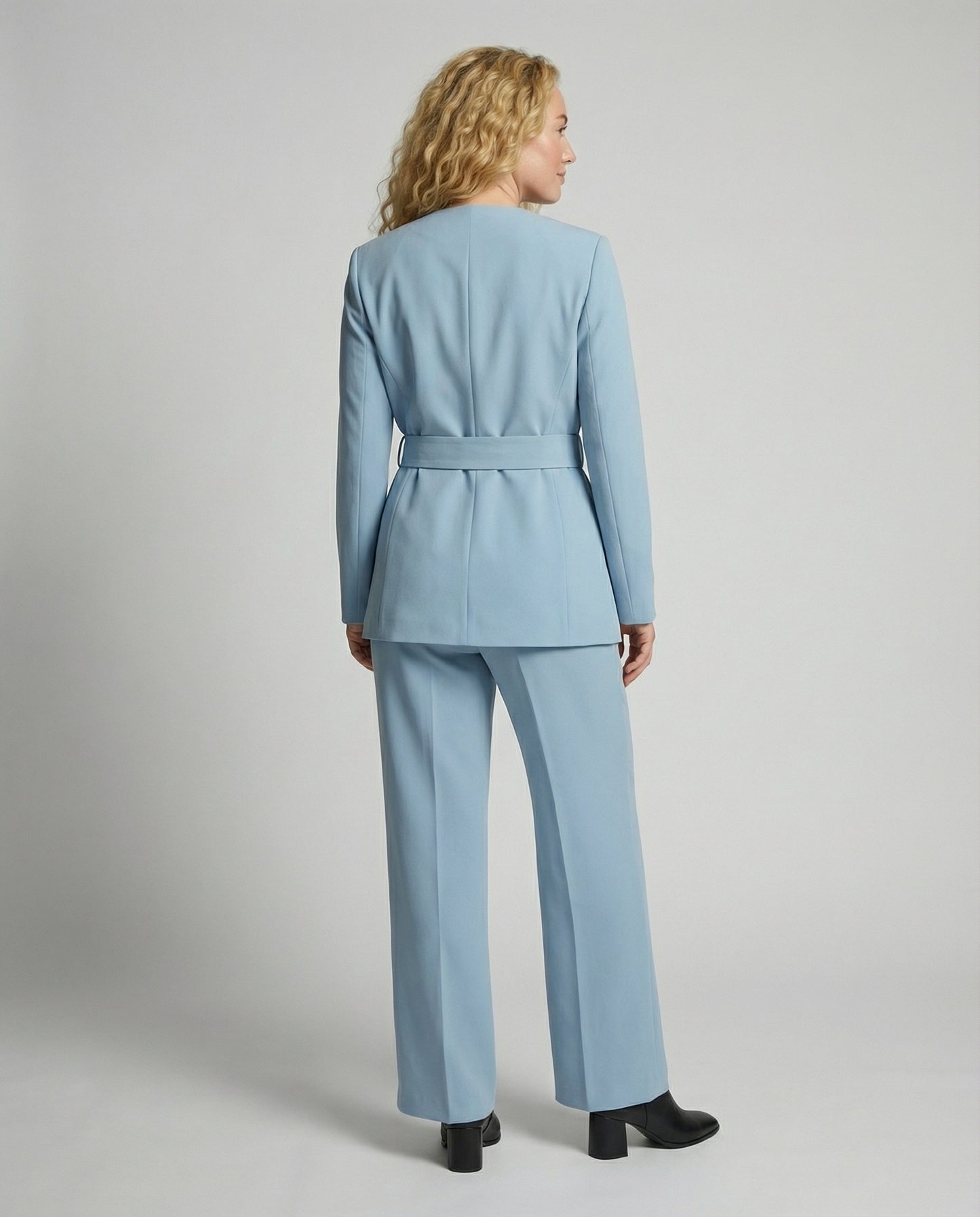 Woman wearing a light blue suit standing against a plain background