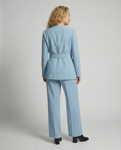 Woman wearing a light blue suit standing against a plain background