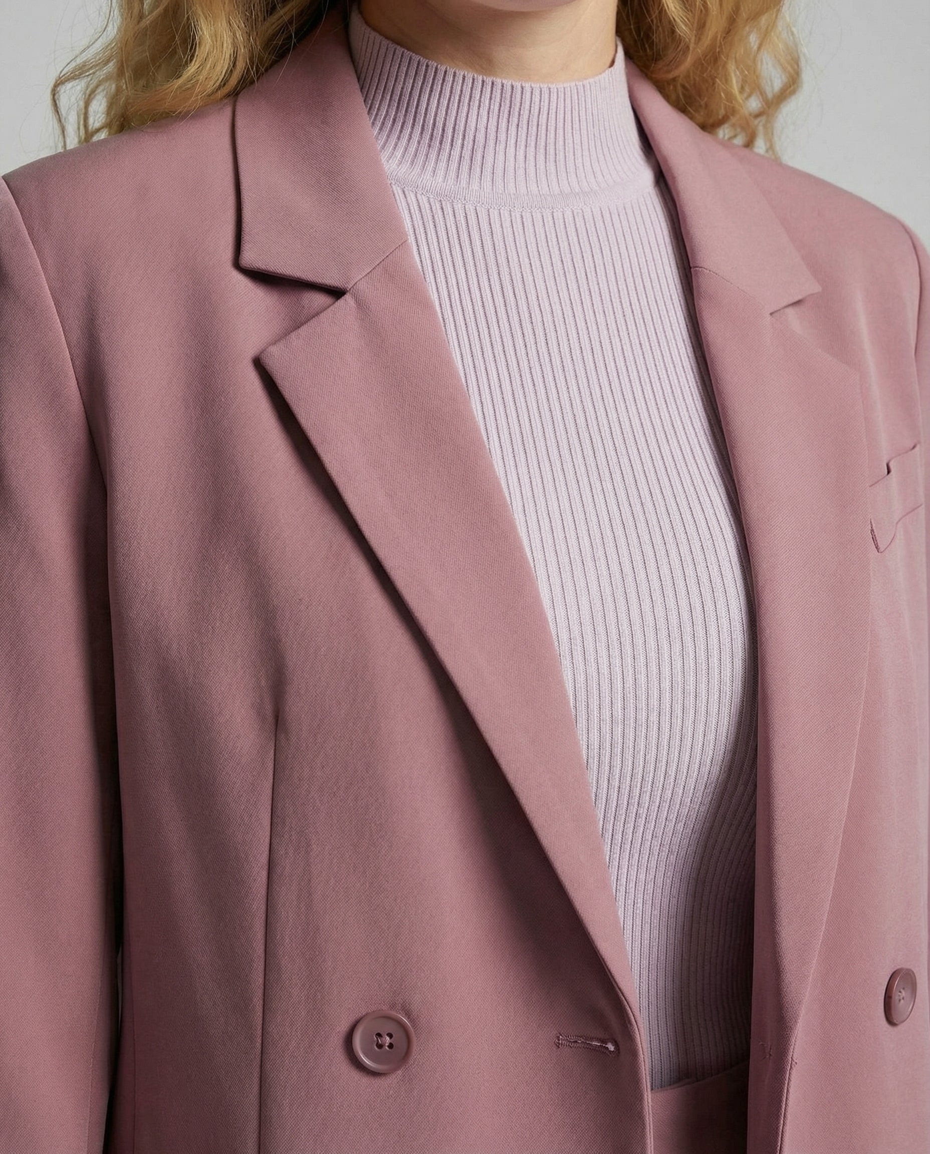 Person wearing a pink blazer over a white ribbed sweater