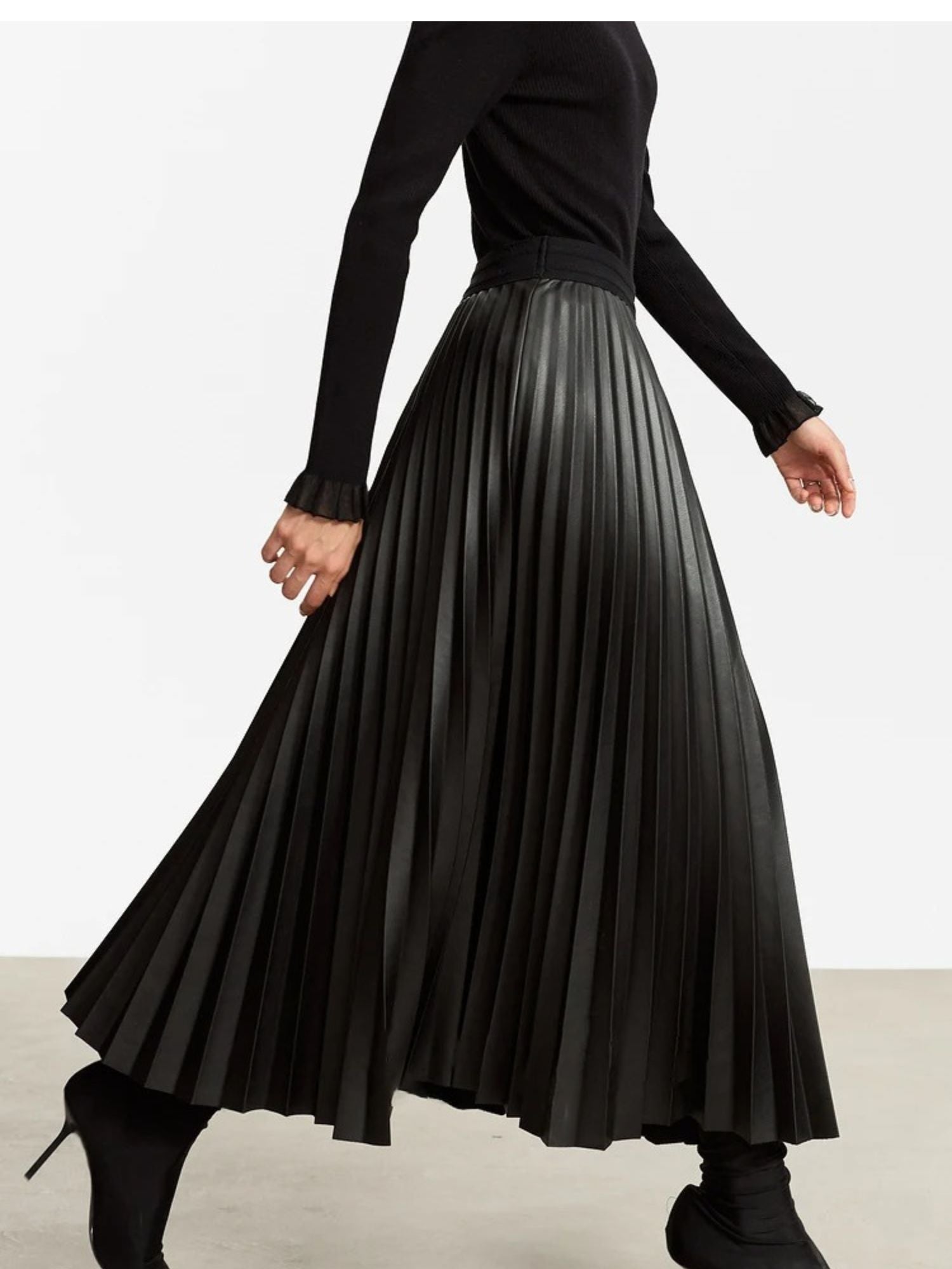 Walking side view of black faux leather pleated midi skirt showcasing flow and movement