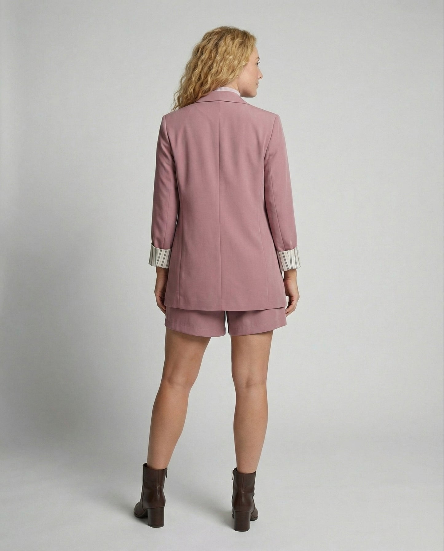 Woman wearing a pink blazer and shorts set on a plain background