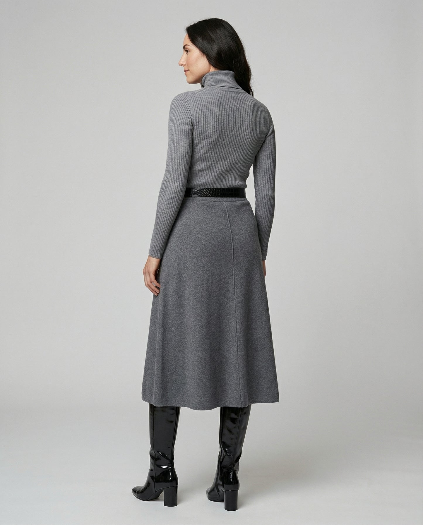 Woman wearing a gray dress with a belt on a plain background