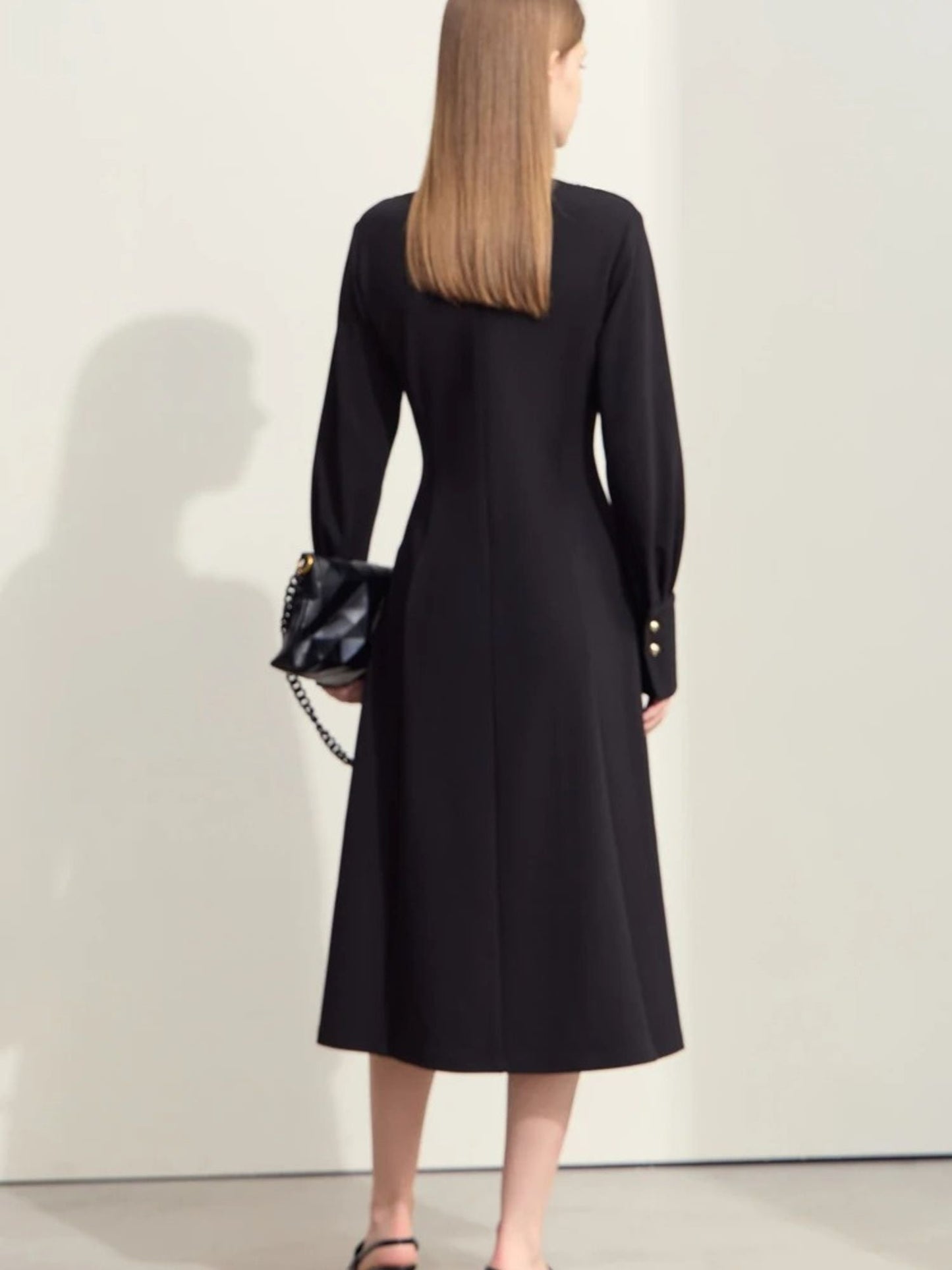 Back view of black midi dress with fitted waist, flared hem, and long sleeves