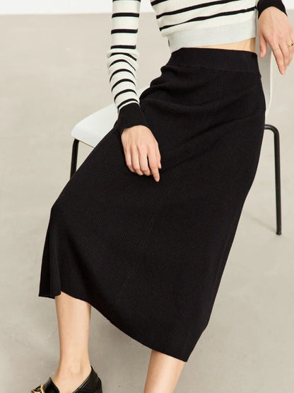 Person wearing a black skirt and striped sweater on a neutral background