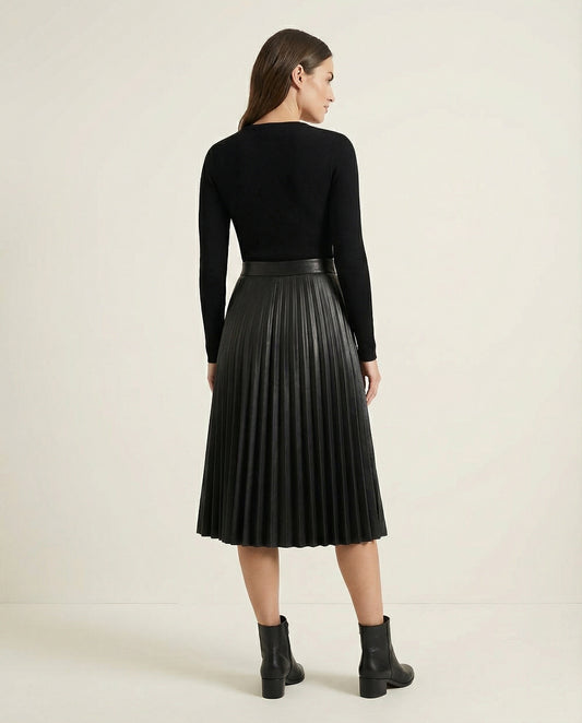 Woman wearing a black pleated skirt and black top on a beige background